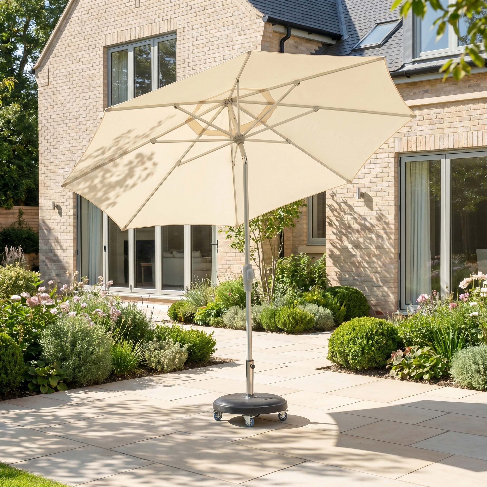 The Zelos 3m Round Parasol with LED Lighting in Cream offers UV protection as it stands on a paved patio in a sunny, landscaped garden beside a modern brick house.