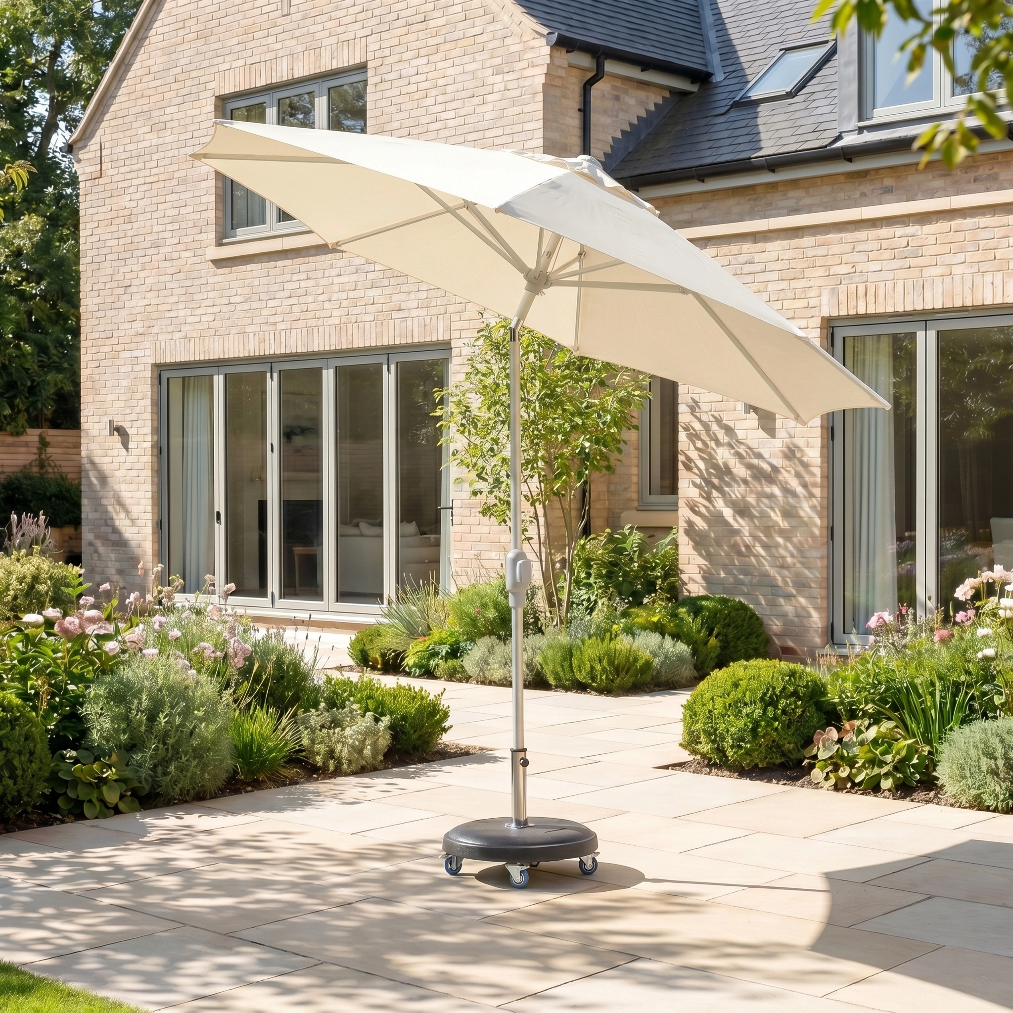 The Zelos 3m Round Parasol with LED Lighting in Cream and UV protection stands on a paved garden patio beside a modern brick house and lush garden.