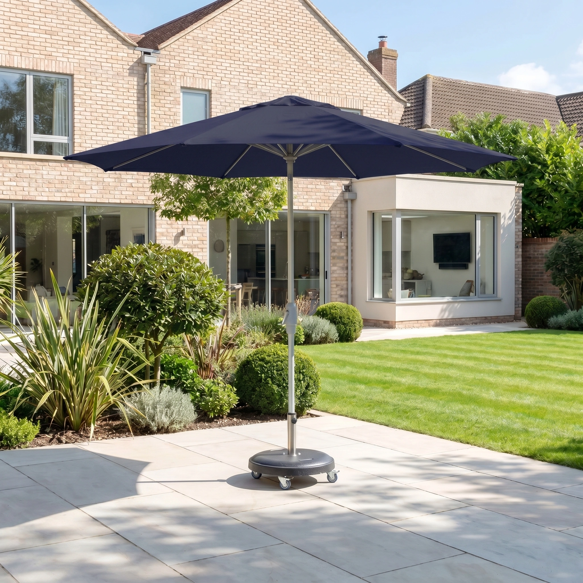 The Zelos 3m Round Parasol with LED Lighting in Navy stands on a paved yard near a modern house with large windows and a green lawn.