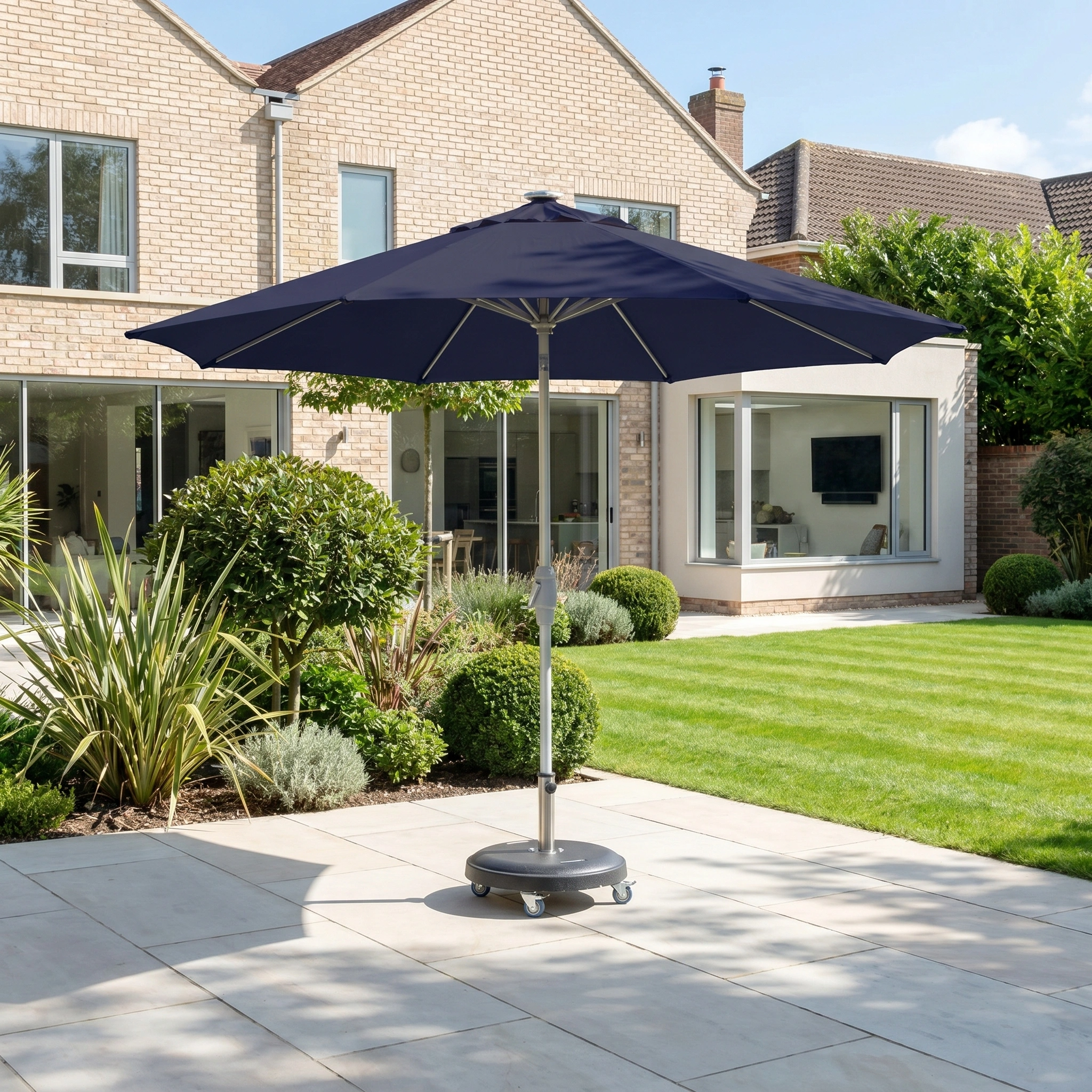 The Zelos 3m Round Parasol with LED Lighting in Navy stands on a tiled terrace by a modern brick house, providing ample shade and stylish UV protection in your sunny backyard.