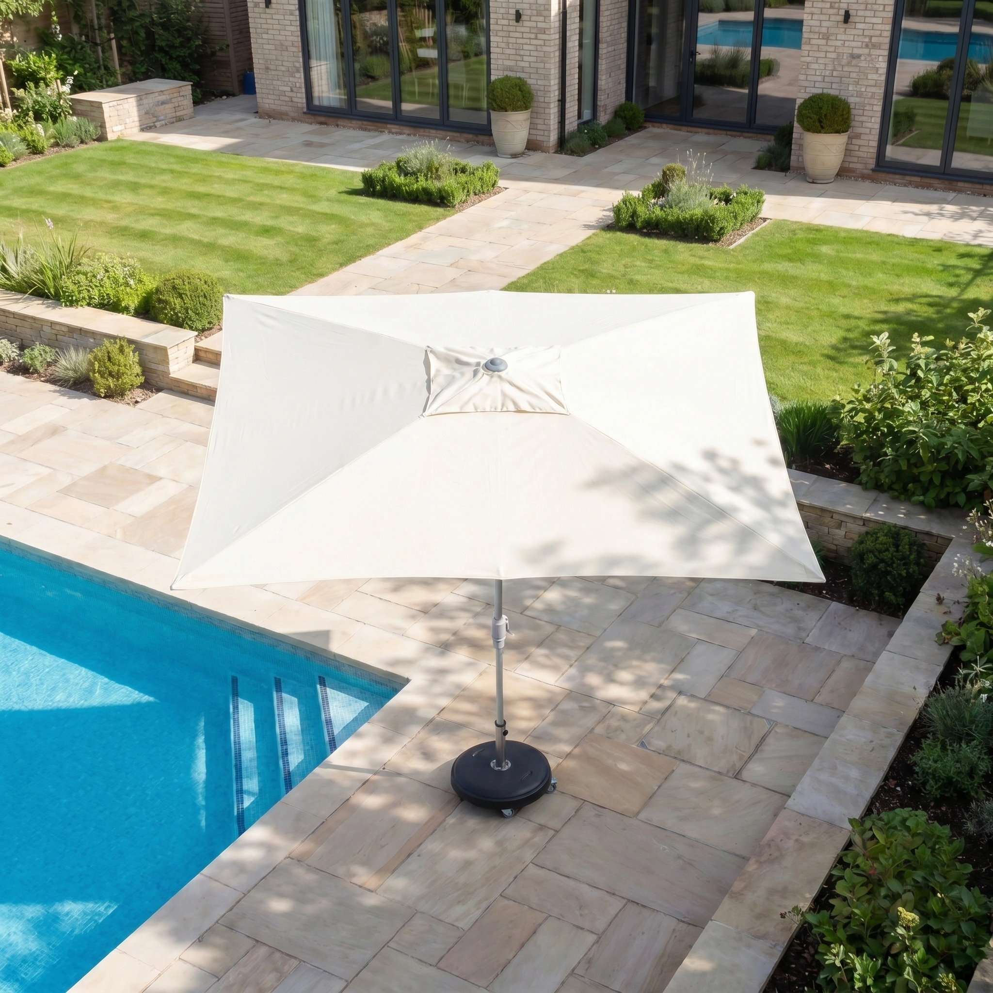 The Zelos 3m x 2m Rectangular Parasol with LED Lighting in Cream stands by a pool on a stone-tiled terrace, providing elegant UV protection in a landscaped garden.