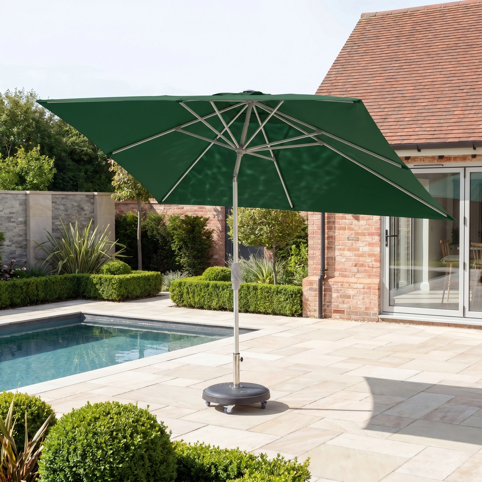 The Zelos 3m x 2m Rectangular Parasol with LED Lighting in Green stands open by a swimming pool, near a brick house and manicured garden, providing ample shade and UV protection.