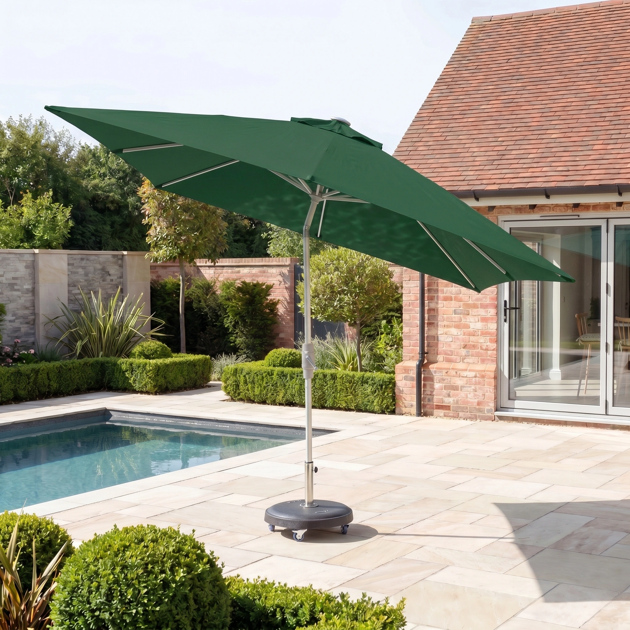 The Zelos 3m x 2m Rectangular Parasol with LED Lighting in Green stands beside the swimming pool.