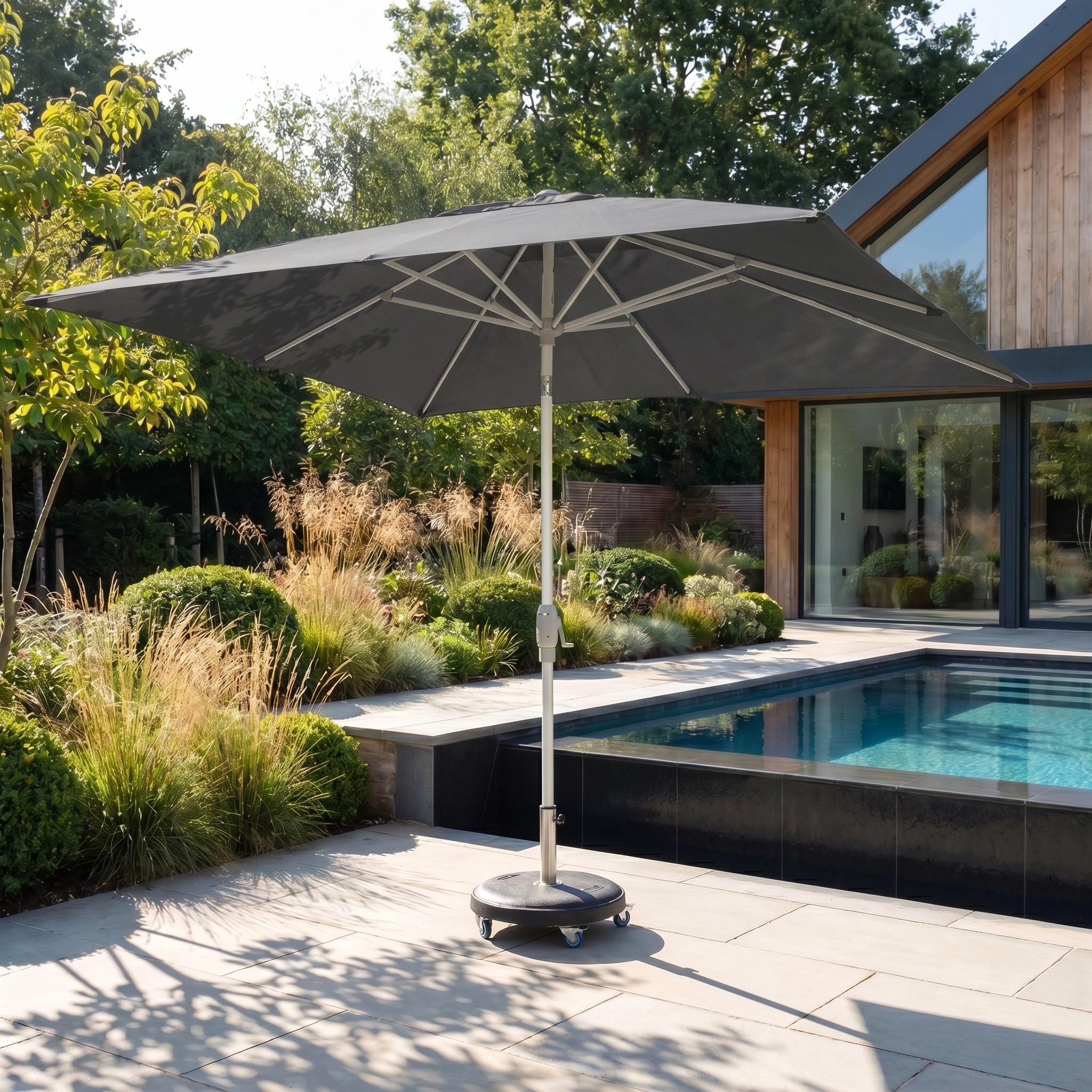The Zelos 3m x 2m Rectangular Parasol with LED Lighting in Grey provides shade for a poolside patio beside a modern house and lush landscaping.