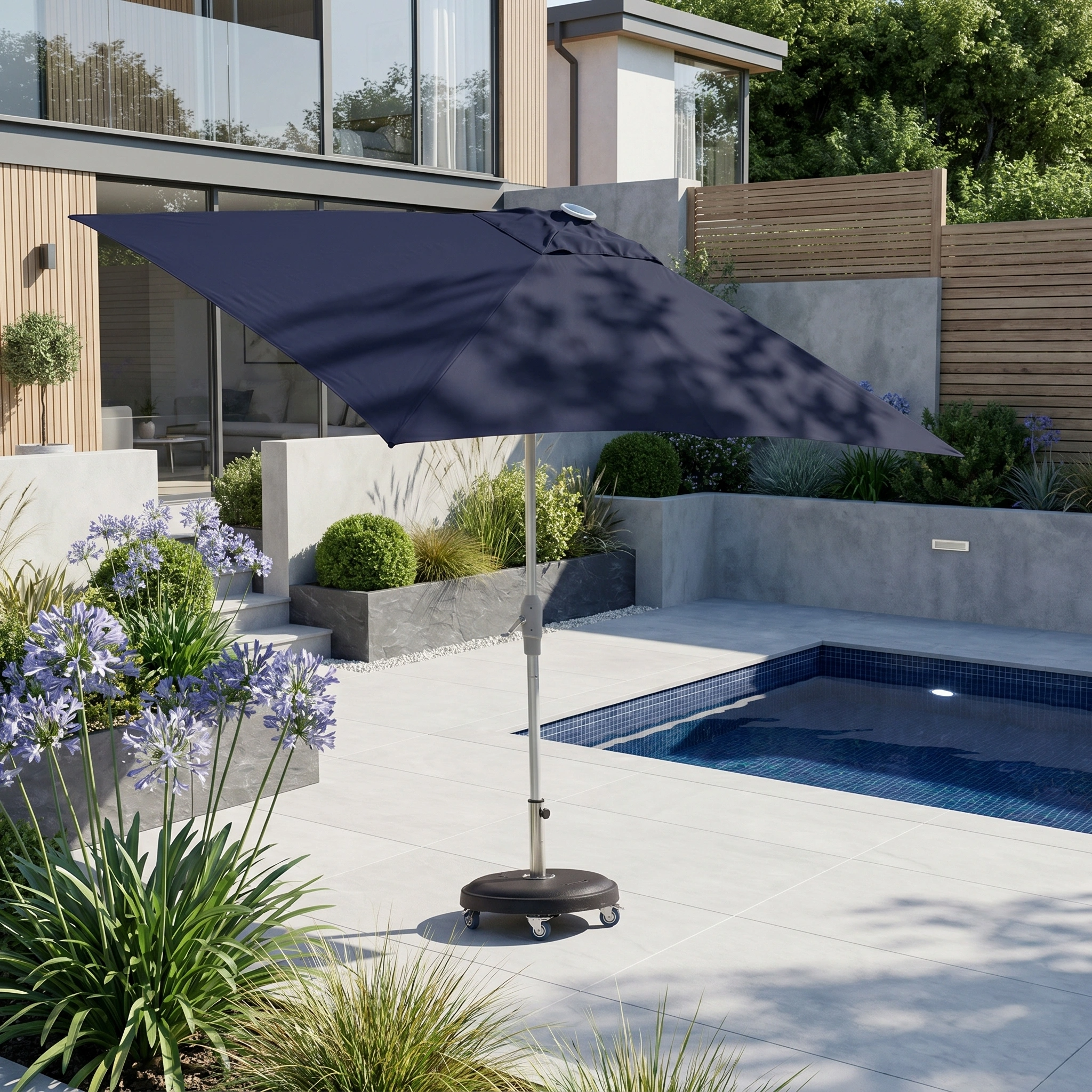 The Zelos 3m x 2m Rectangular Parasol with LED Lighting in Navy stands by a modern backyard pool, offering UV protection and style amid lush plants and thoughtful landscaping.