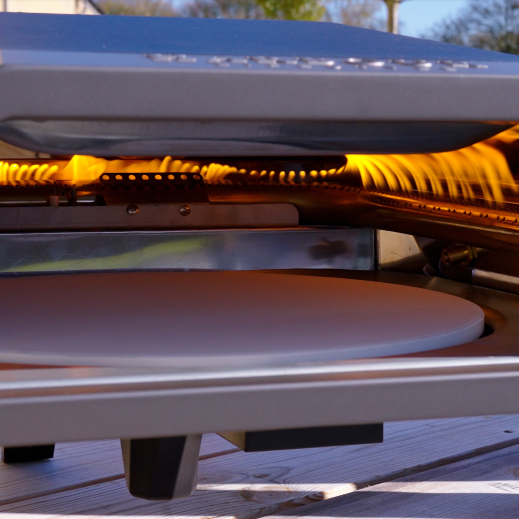 Close-up of an open Juno Pro 16" Gas Pizza Oven with visible flames heating the interior and a flat stone slab inside, perfect for making a 60-second stone-baked pizza.
