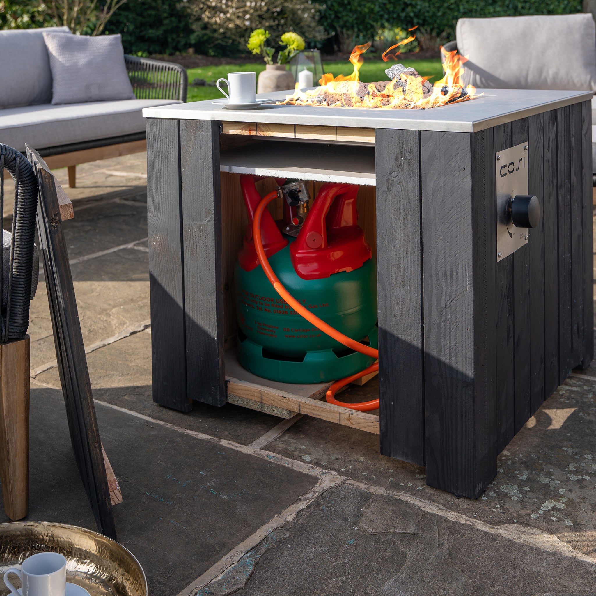 The Cosi - Cosicube 70 Black Fire Pit is an outdoor table with a sleek design, featuring an open compartment to neatly store a propane gas tank underneath.