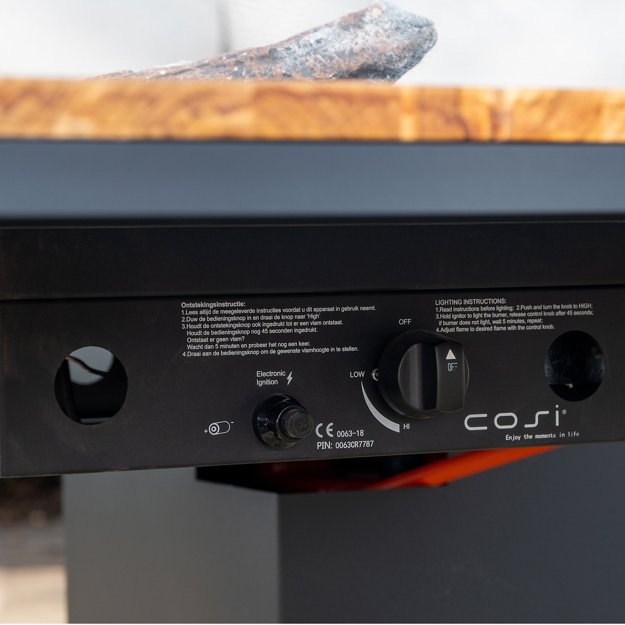 Close-up of the Cosi - Cosiloft 100 Black and Teak Fire Pit Table's control panel, featuring adjustment knobs and instruction labels, complemented by its sleek Teak Wood finish that highlights its weatherproof design.