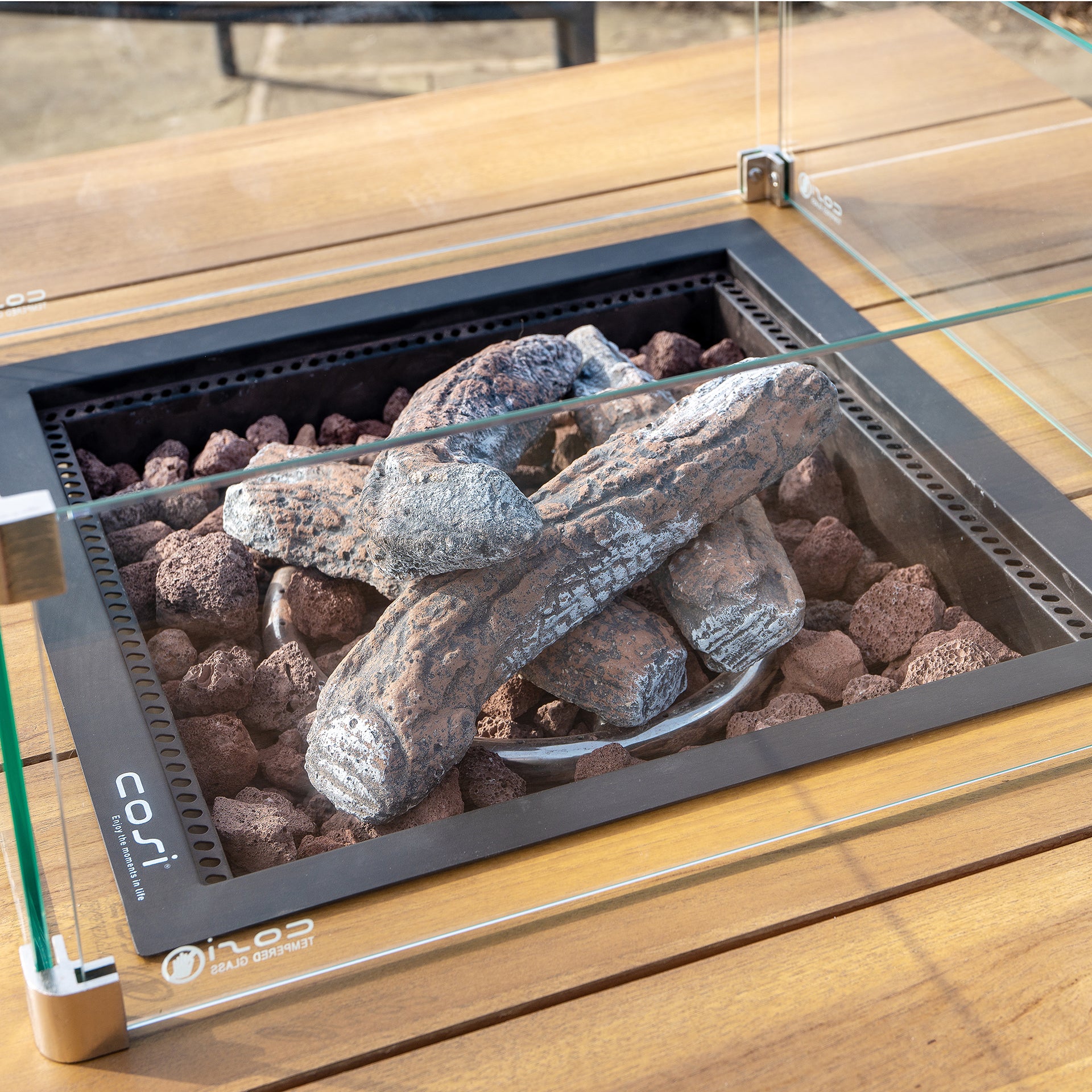Weatherproof Cosi Cosiloft 100 Black and Teak Fire Pit Table features a gas fire pit with artificial logs, lava rocks, and elegant glass panels.