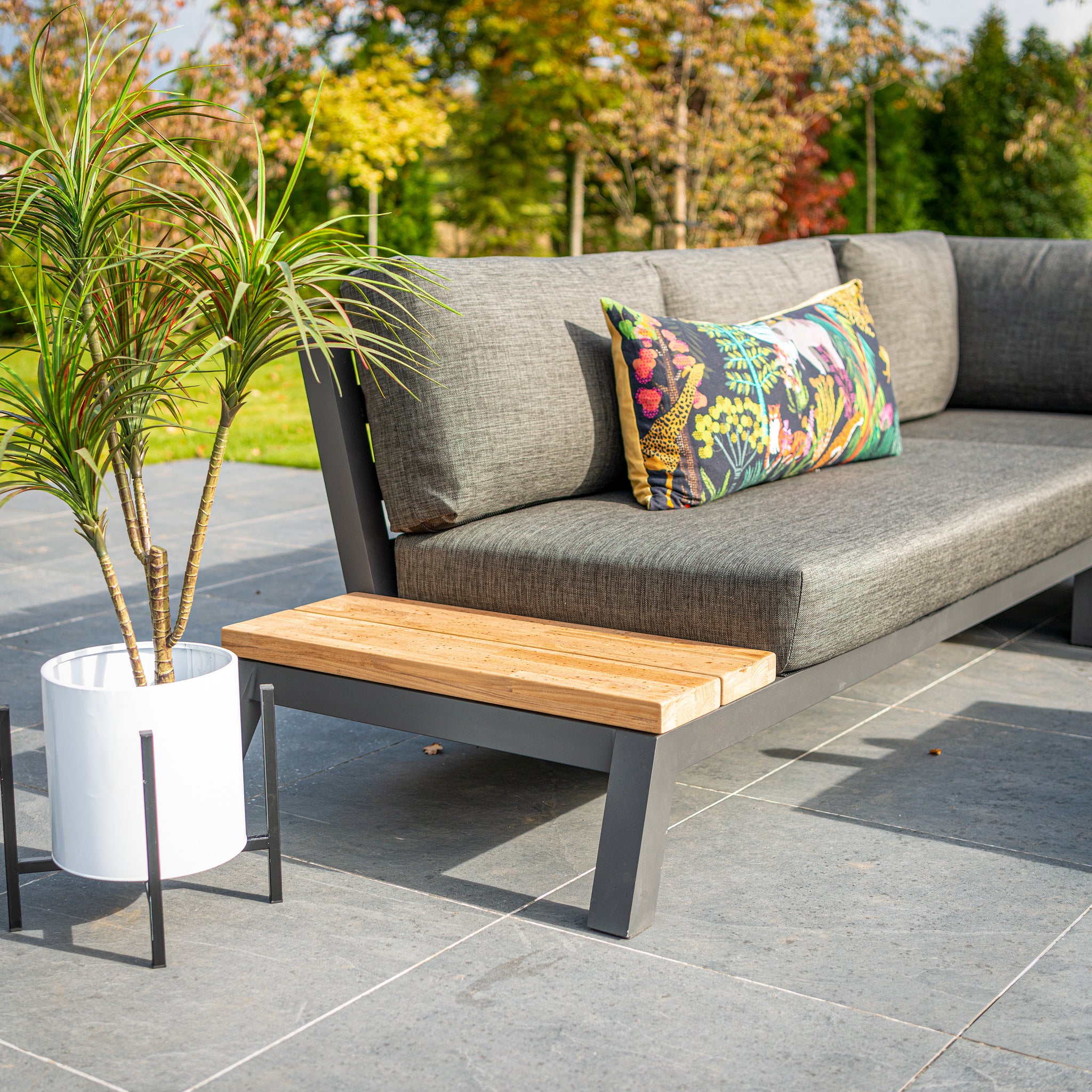 Outdoor patio with Empire Large Corner Group Set featuring gray olefin fabric, colorful cushions, and a potted plant on a tiled floor.