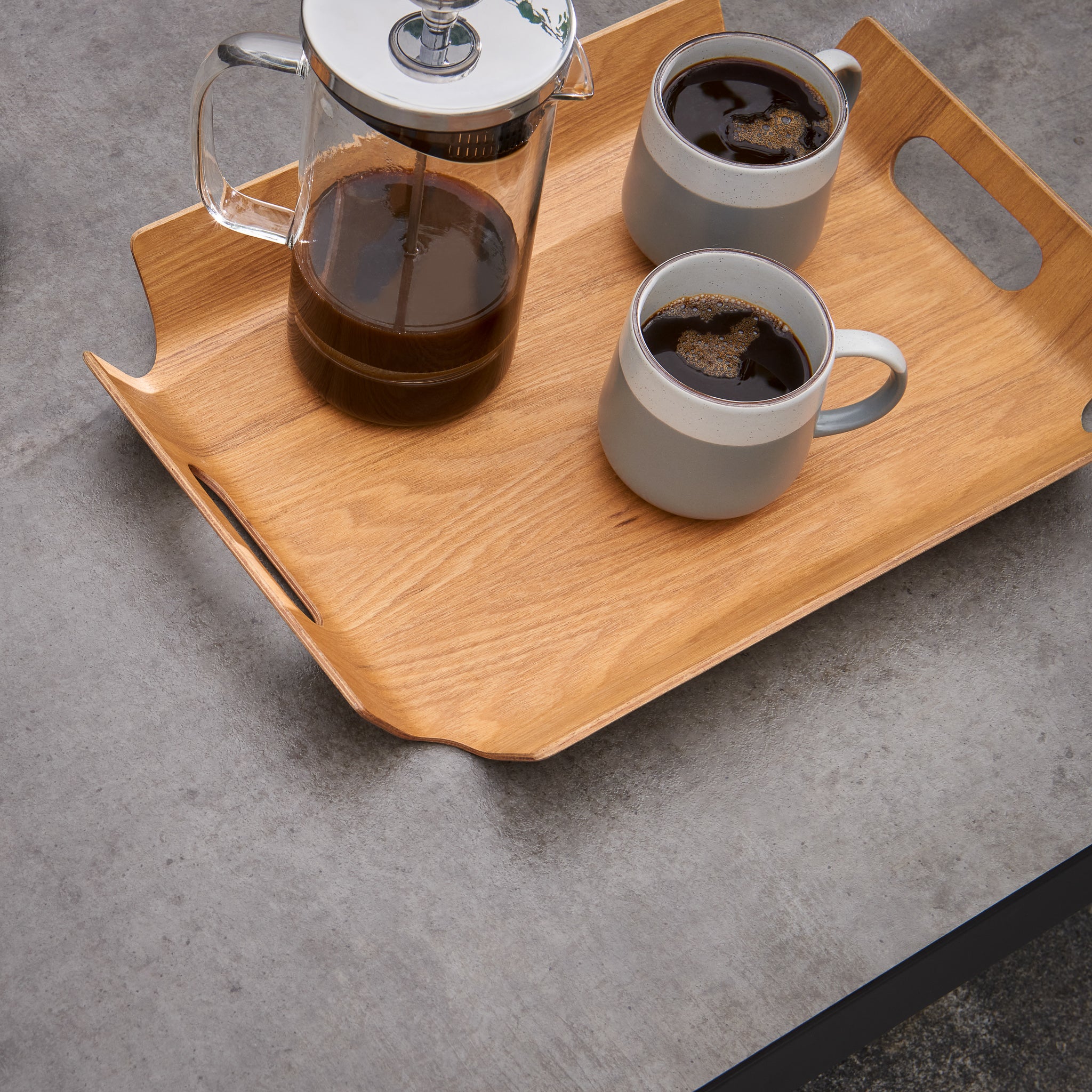 A wooden tray with a French press and two cups of coffee sits elegantly on an Iconic HPL Coffee Table in Anthracite, gracing the grey countertop.