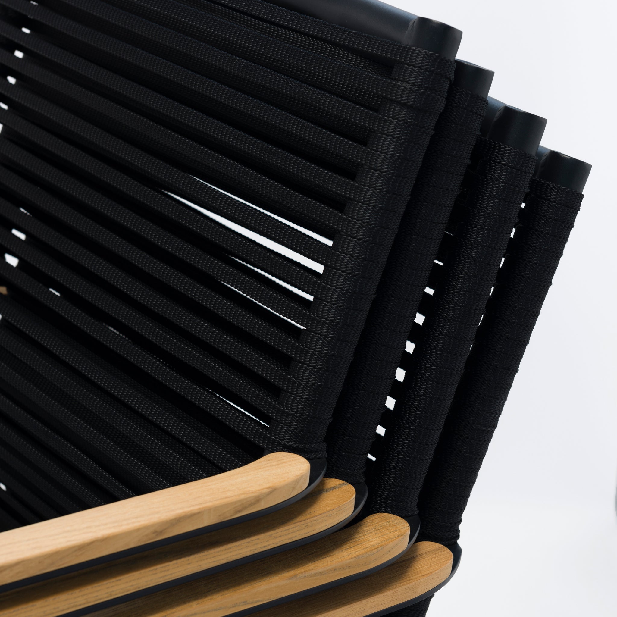 Close-up of a stack of black folding chairs with wooden armrests on a white background, perfect for complementing the Portland 4 Seat Round Dining Set with Teak Table in Charcoal.