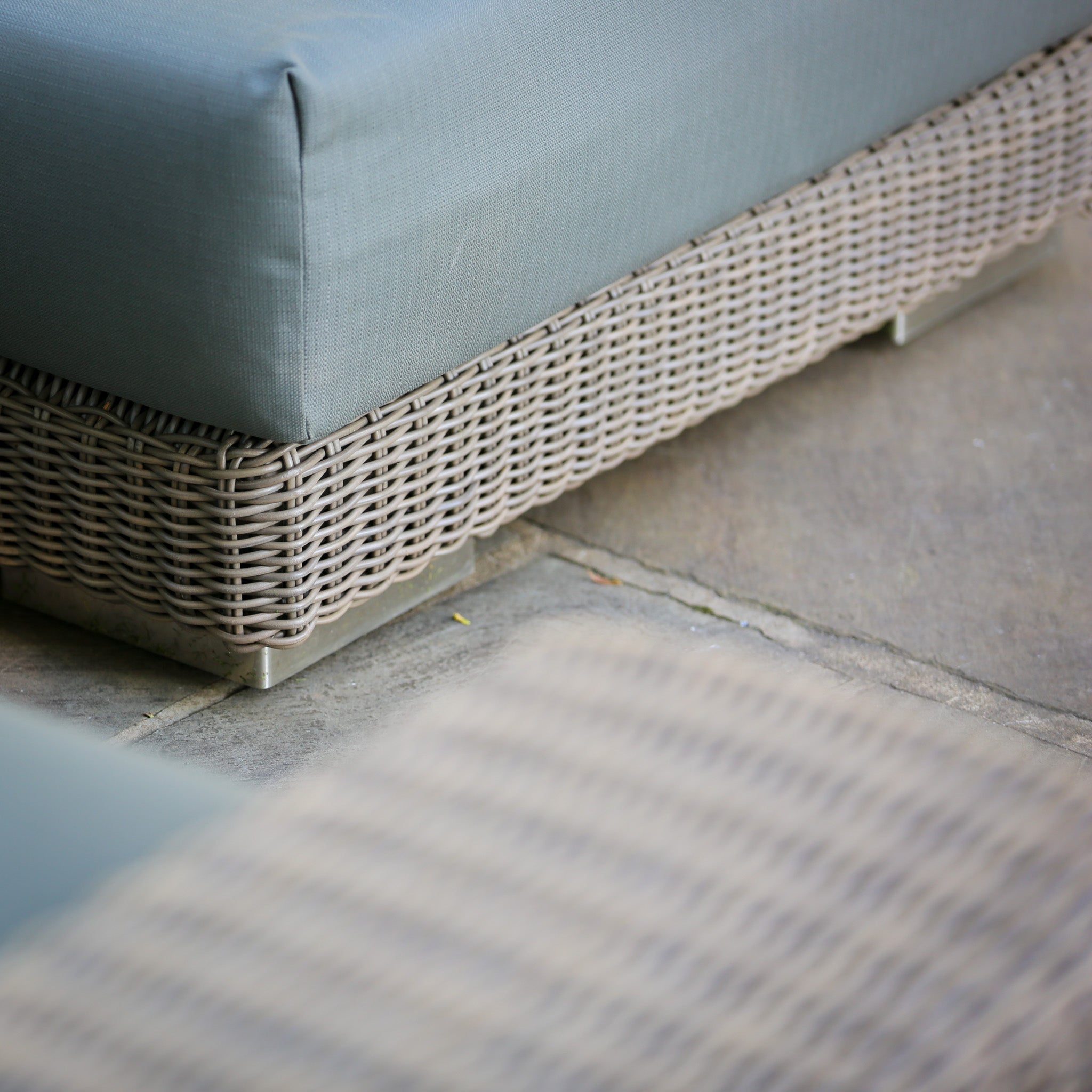 Close-up of the Kingston 3 Seat Sofa Set with gray cushions, crafted in light brown Hularo wicker, on a stone patio.