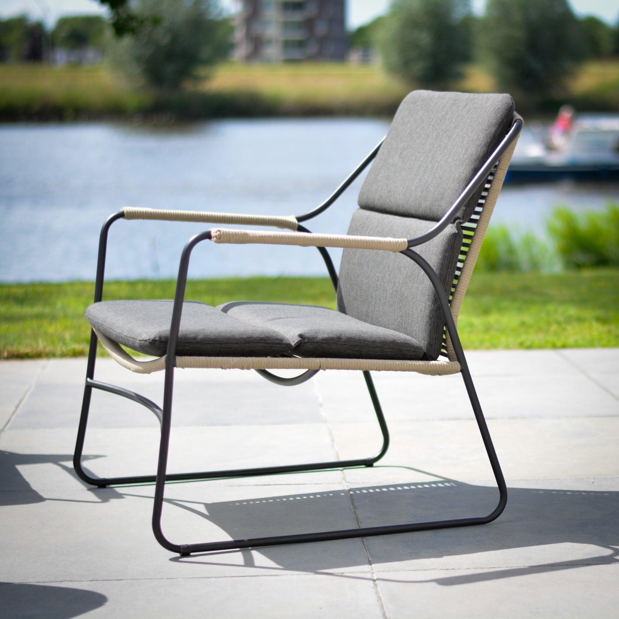 The Scandic 2 Seat Sofa Set features a stainless steel frame and Olefin all-weather gray cushions, ideal for a patio overlooking a grassy area and water—perfect for fans of Scandic garden furniture.
