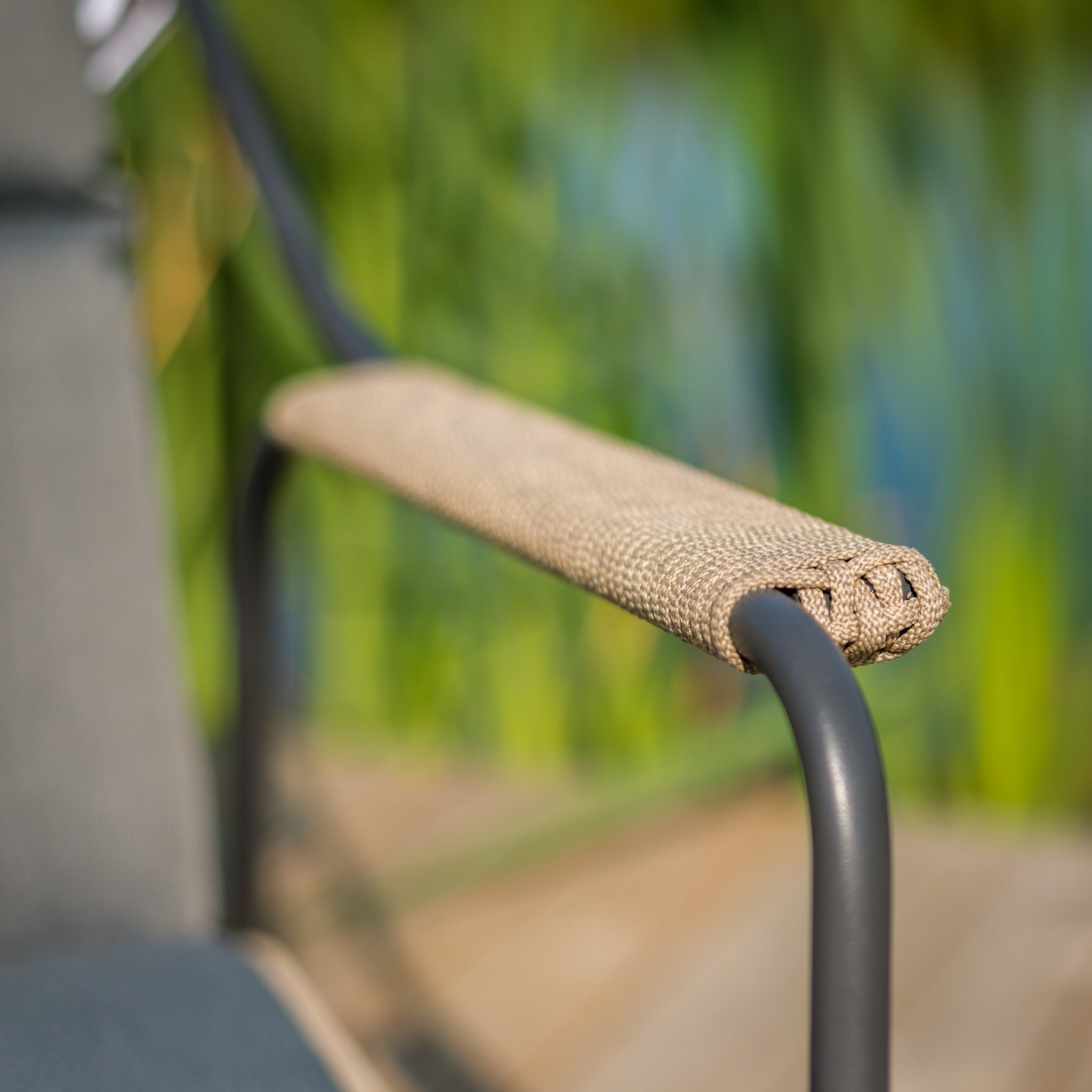 Close-up of a Scandic 2 Seat Sofa armrest in beige woven fabric on a sleek stainless steel frame, with blurred greenery in the background.