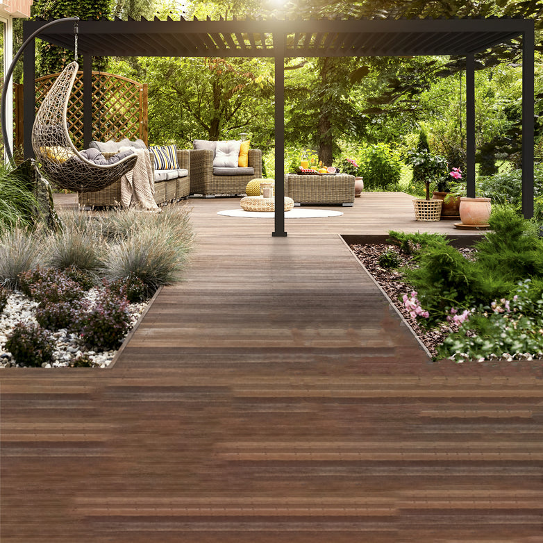 A wooden deck with lounge furniture, a hanging chair, and a garden area filled with plants and flowers is beautifully sheltered by the elegant 3m x 6m Rectangular Pergola with 4 Drop Sides in Grey.