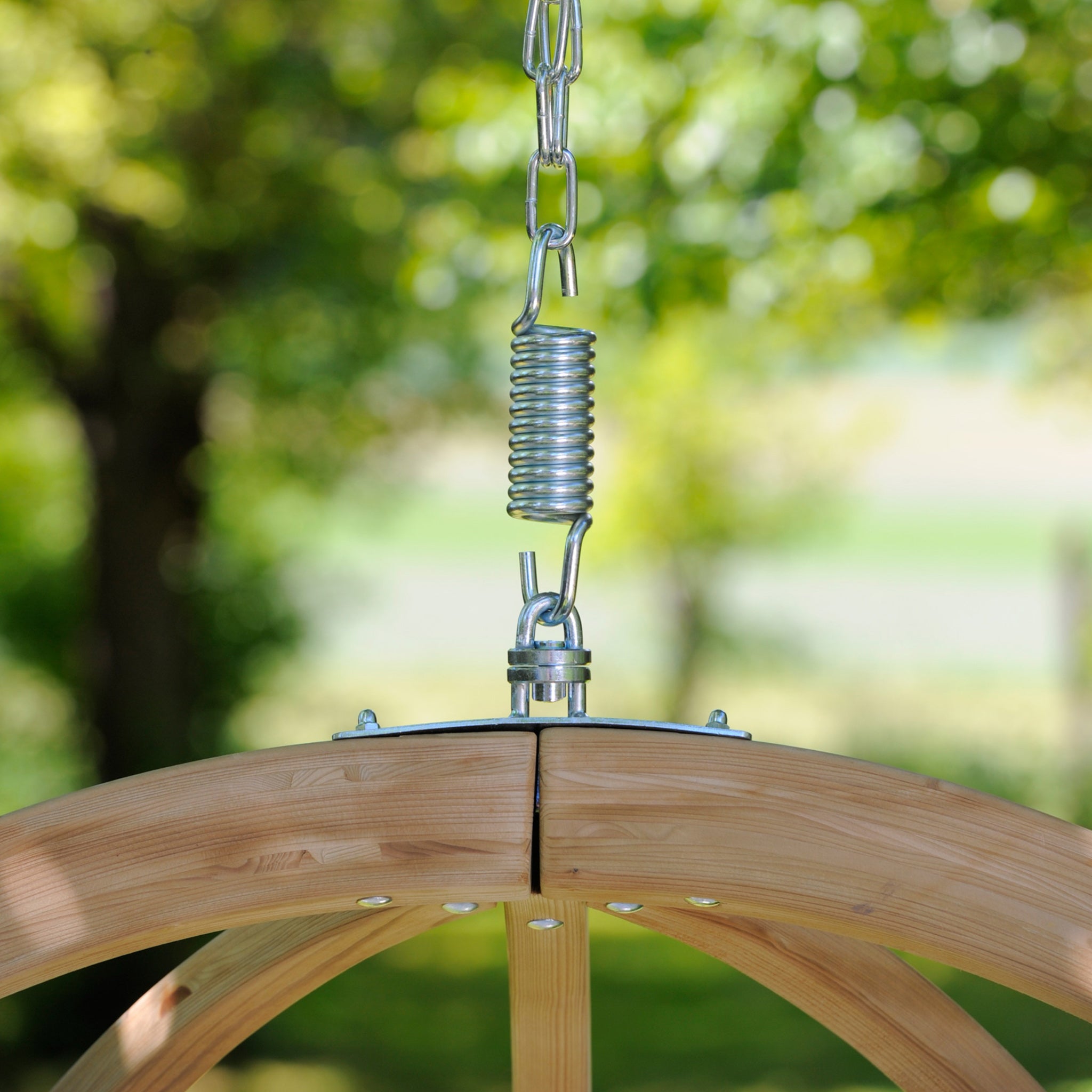 Close-up of the Natura Globo Single Hanging Chair attached with a metal spring, set against a blurred background of trees and greenery, exemplifying stylish furniture perfect for both indoor and outdoor living spaces.