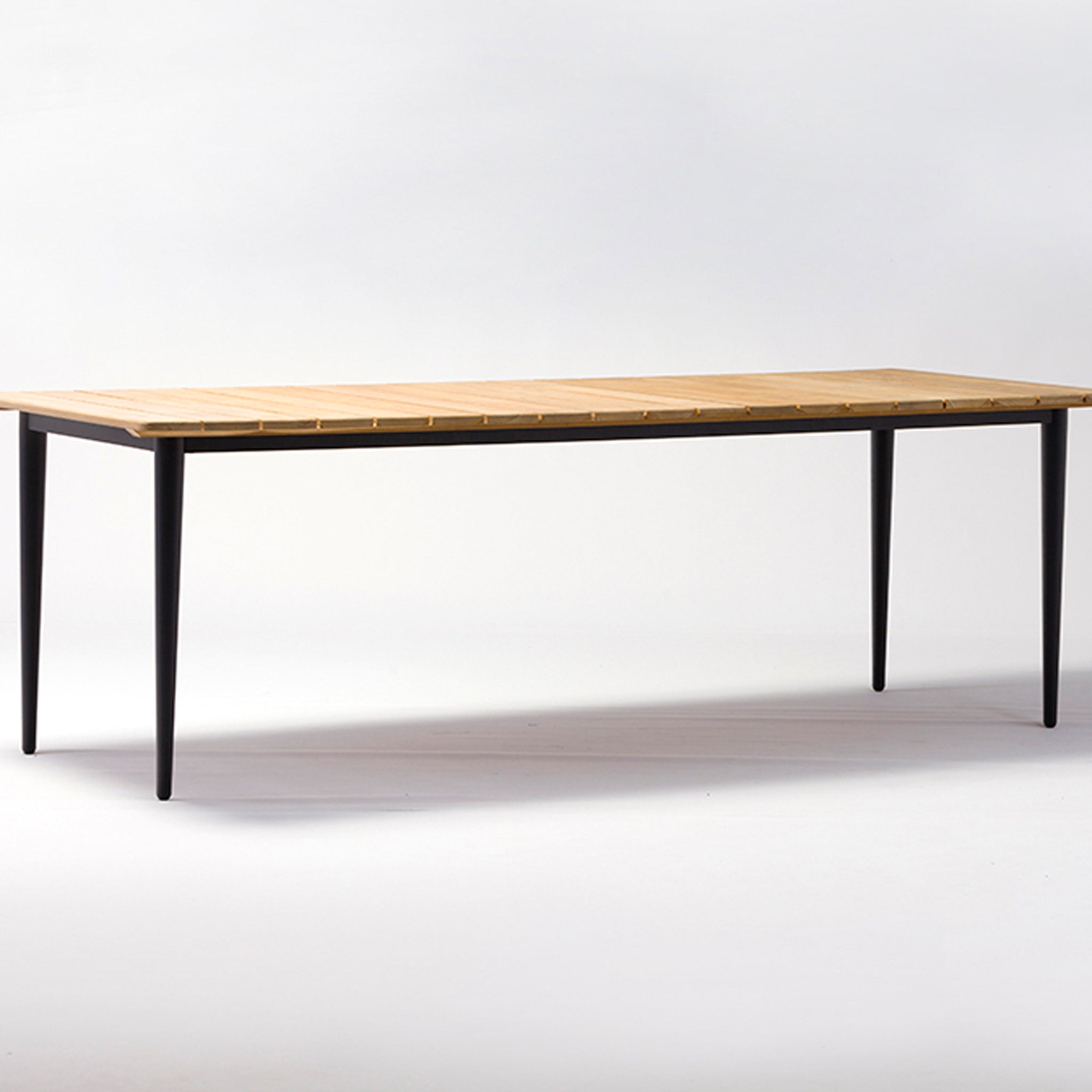 A teak rectangular dining table with black tapered legs, part of the Kalama 8 Seat Dining Set in olive green, against a white background.