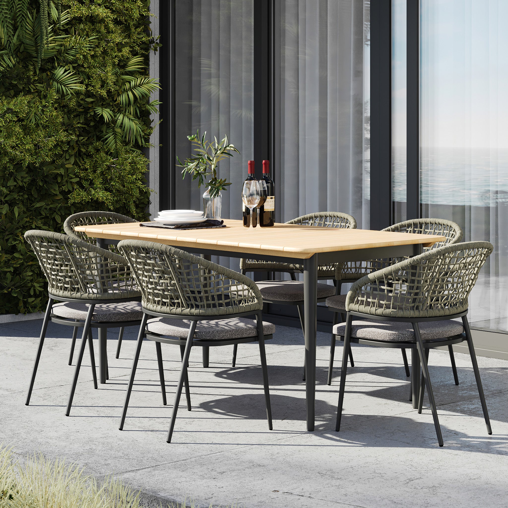 The Kalama 6 Seat Rectangular Dining Set in Olive Green features a teak table, six woven chairs, two wine bottles, glasses, and lush plants in the background.