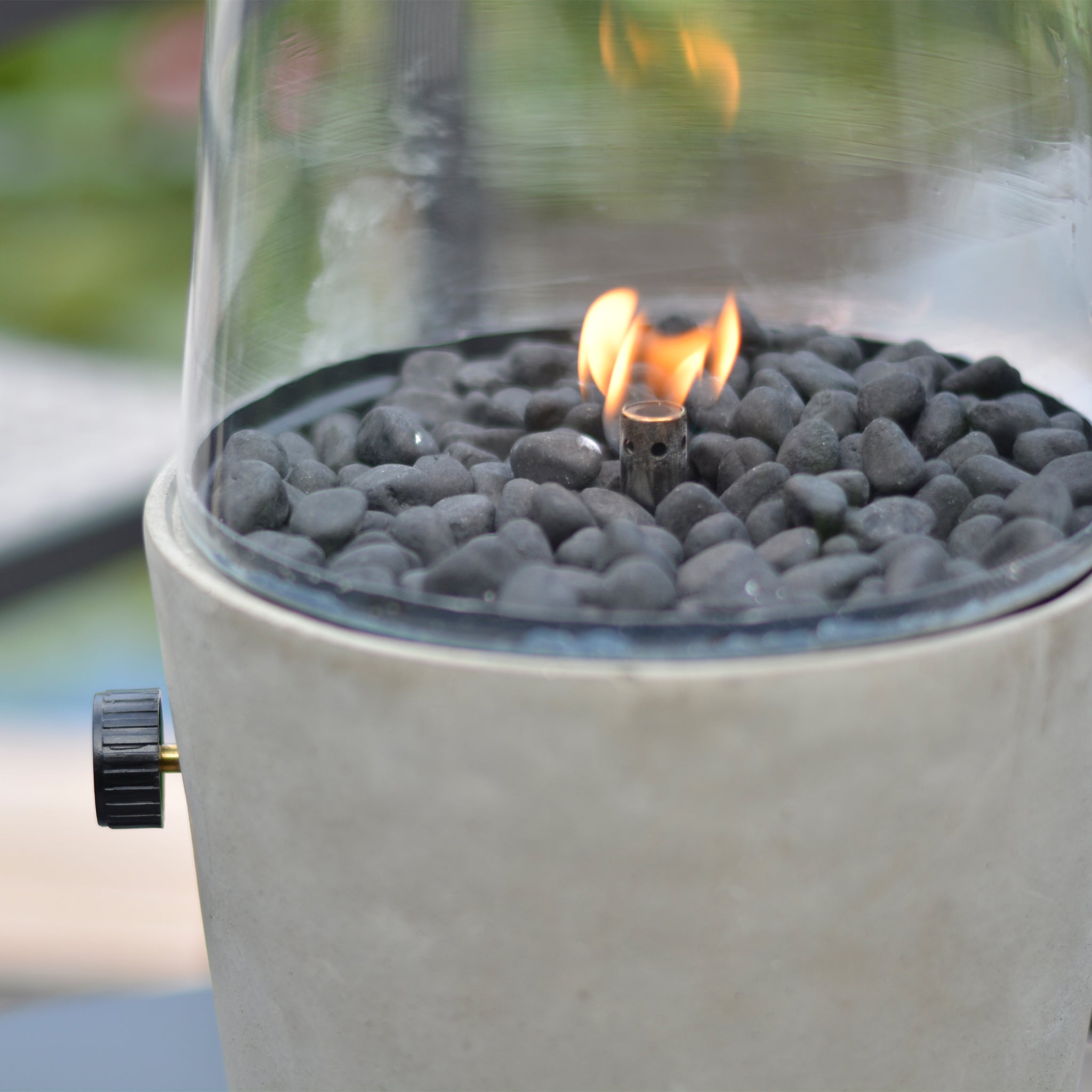 A small stone fire pit with a glass cover, black stones, and a gentle flame exudes an elegant concrete effect finish reminiscent of the Cosi - Cosicement Round Fire Lantern.