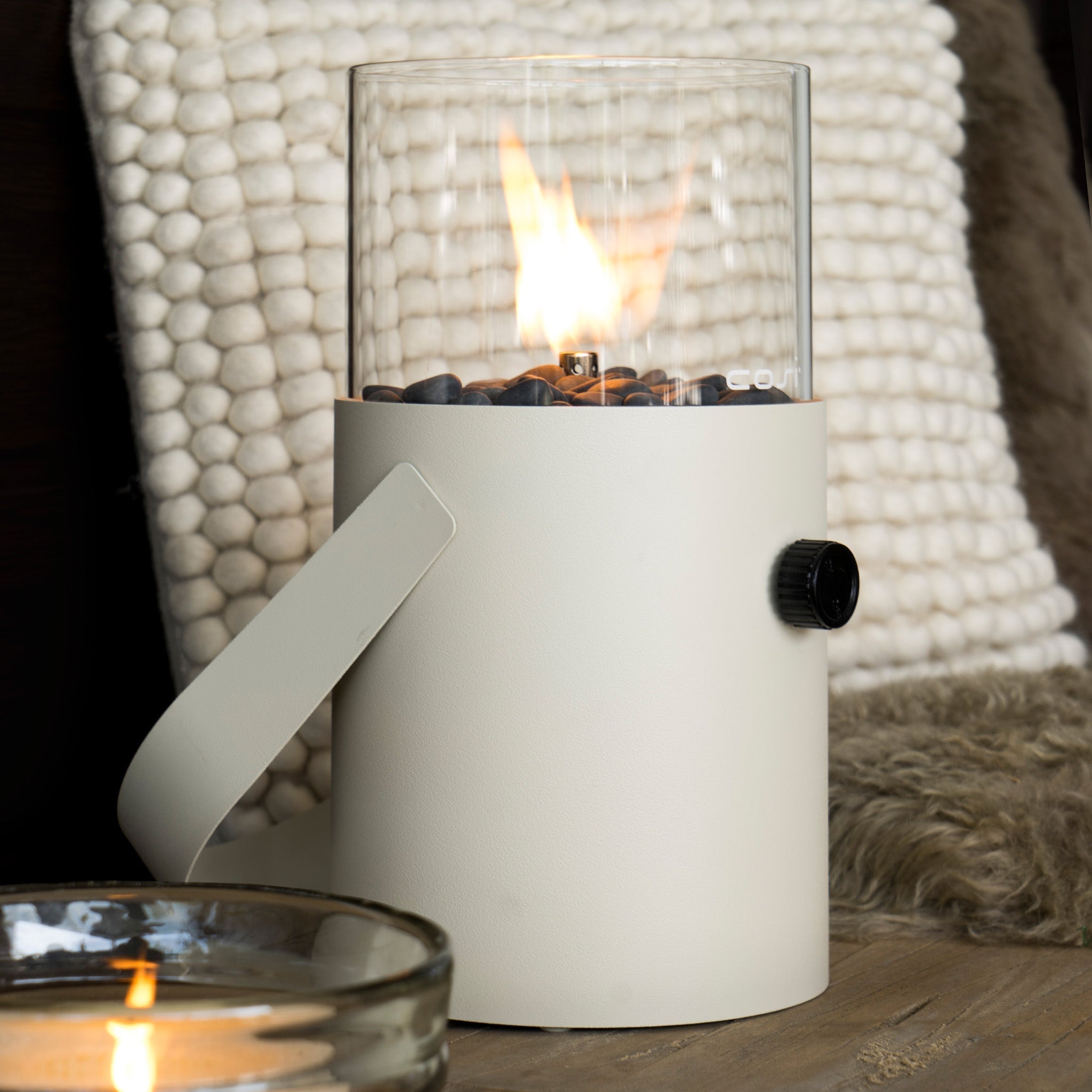 The Cosi - Cosiscoop Fire Lantern in Ivory, featuring a flame in a glass cylinder and surrounded by black stones, brings elegance to any space.