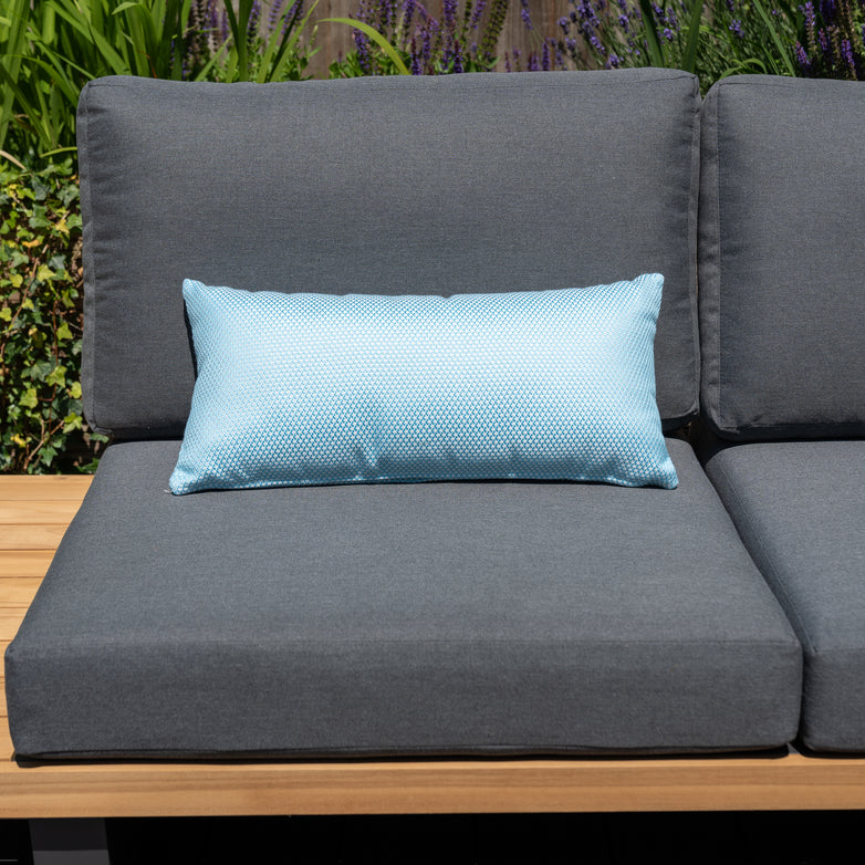 Gray outdoor sofa with matching solution-dyed acrylic cushions, featuring a light blue lumbar pillow in the middle, set against a lush garden backdrop. Enhance it further with Agora Scala Celeste Bolster Scatter Cushions - 60cm x 30cm for added comfort and style.