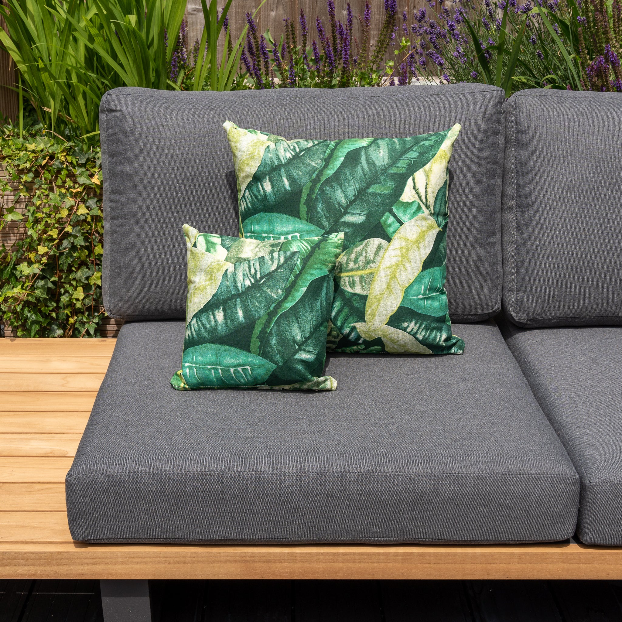 Gray outdoor sofa with wooden accents featuring two Acrisol Amazonia Verde Small Scatter Cushions (25cm x 25cm) in a garden setting, crafted from durable solution-dyed acrylic.