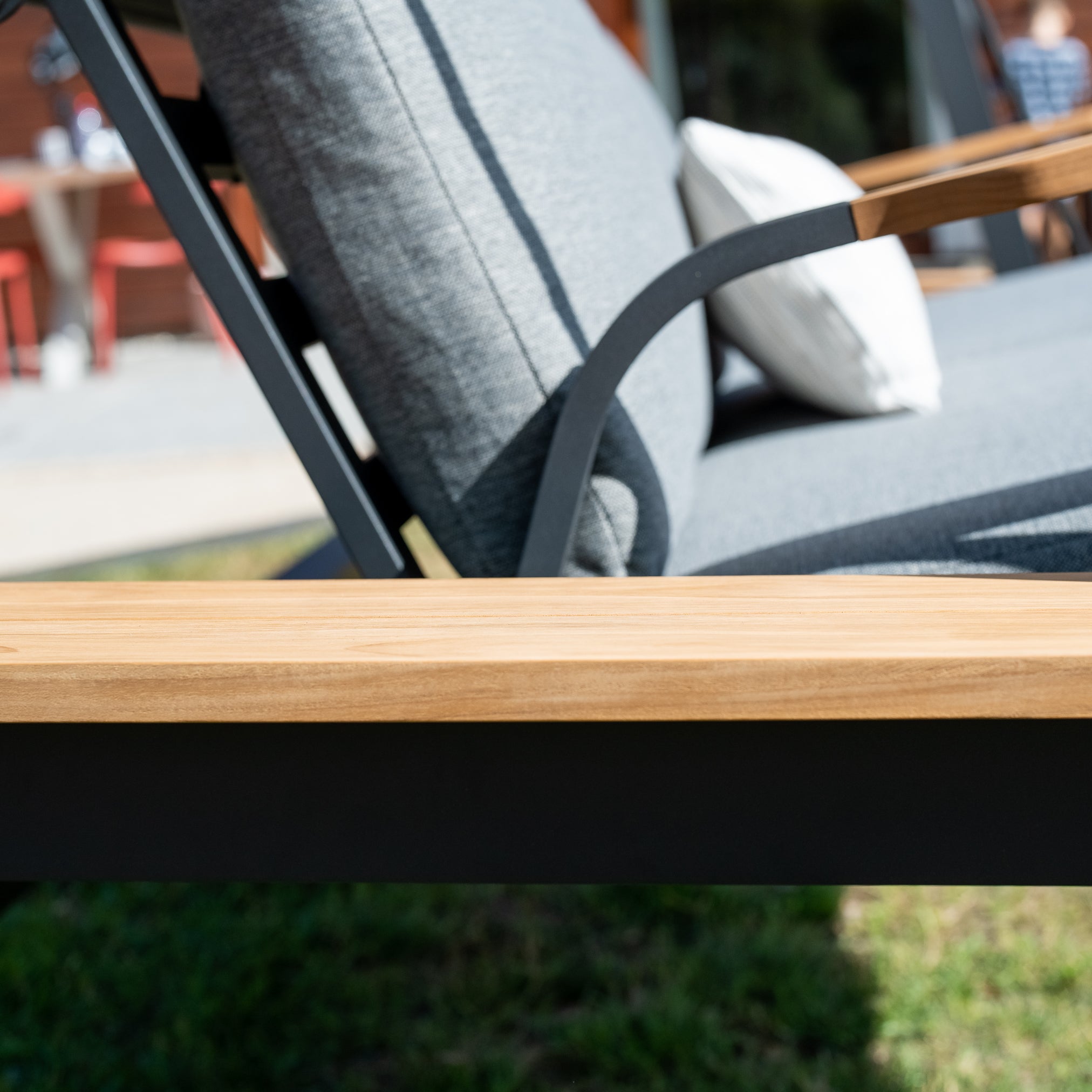 Close-up of a wooden armrest on the Lima Deluxe Aluminium Swing Seat in Washed Grey, a stylish gray outdoor lounge chair made with durable Olefin material. A pillow and blurred background are visible.