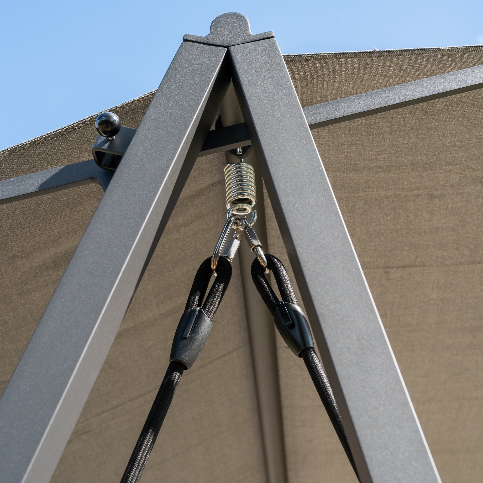 Close-up of a metallic support frame with spring and rope attachments for the Lima Deluxe Aluminium Swing Seat in Washed Grey against a clear blue sky.