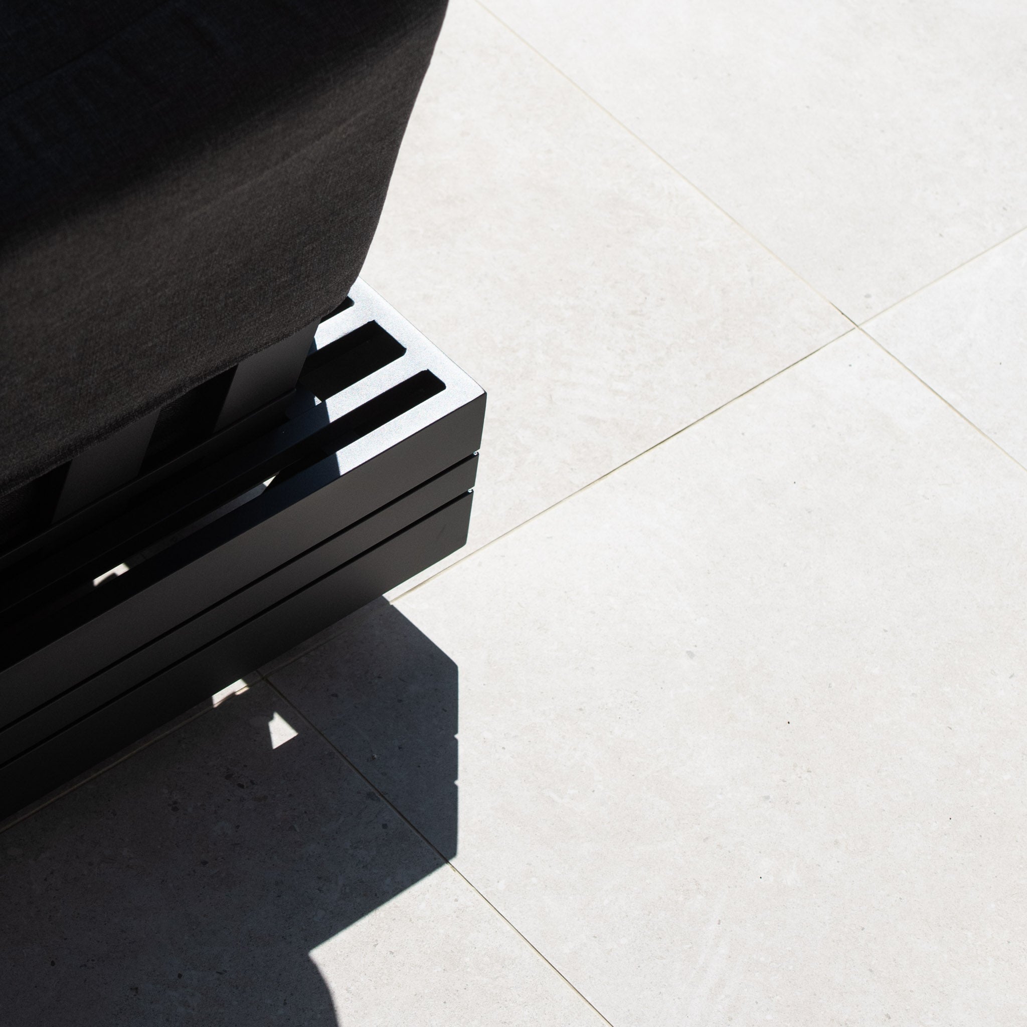 Close-up of the Panama Luxury Outdoor Large Corner Group Set in Charcoal's metal base casting a shadow on light-colored tile flooring, exemplifying the elegance of luxury outdoor furniture.
