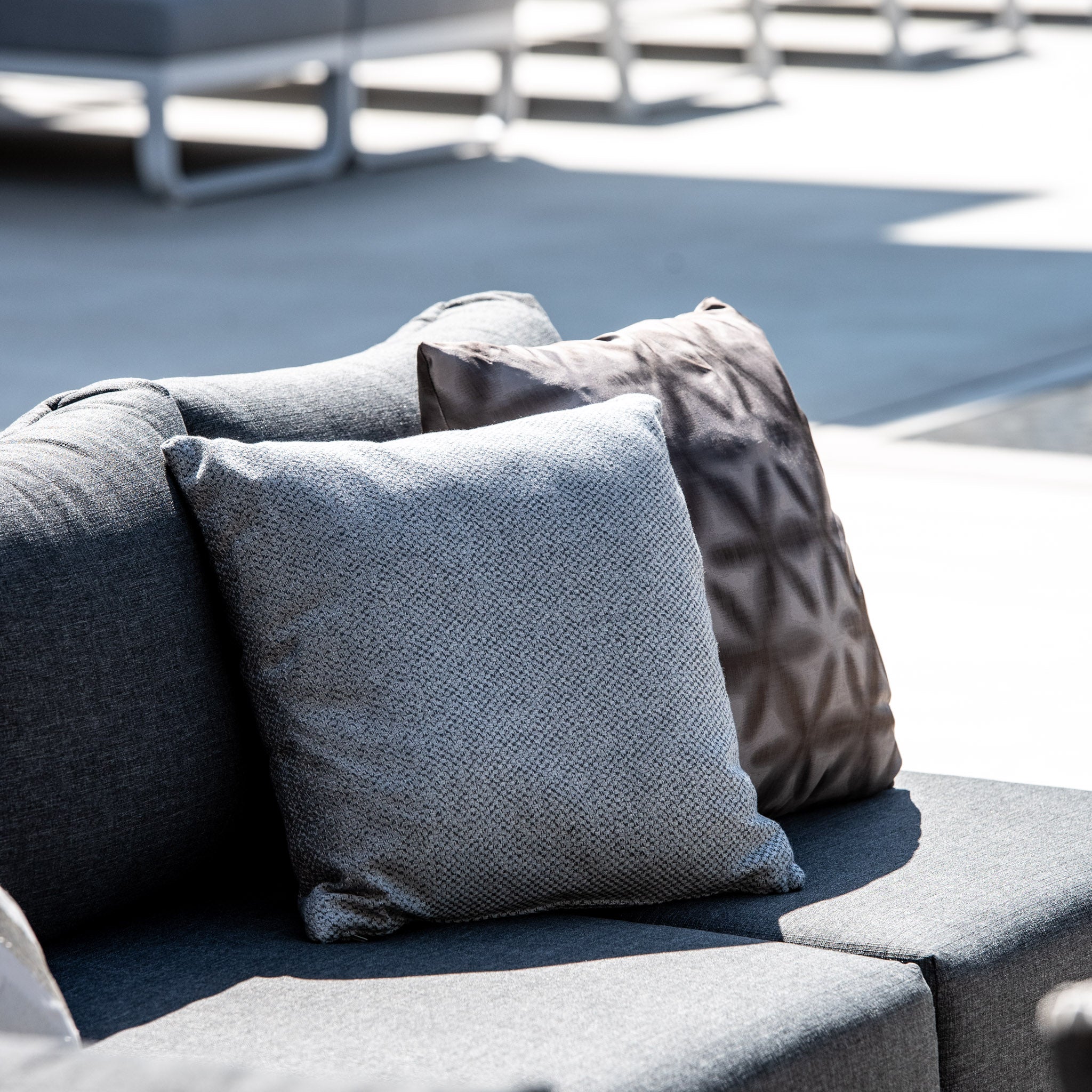 Close-up of charcoal gray pillows and patterned cushions on the Panama Luxury Outdoor Large Corner Group Set under bright sunlight.