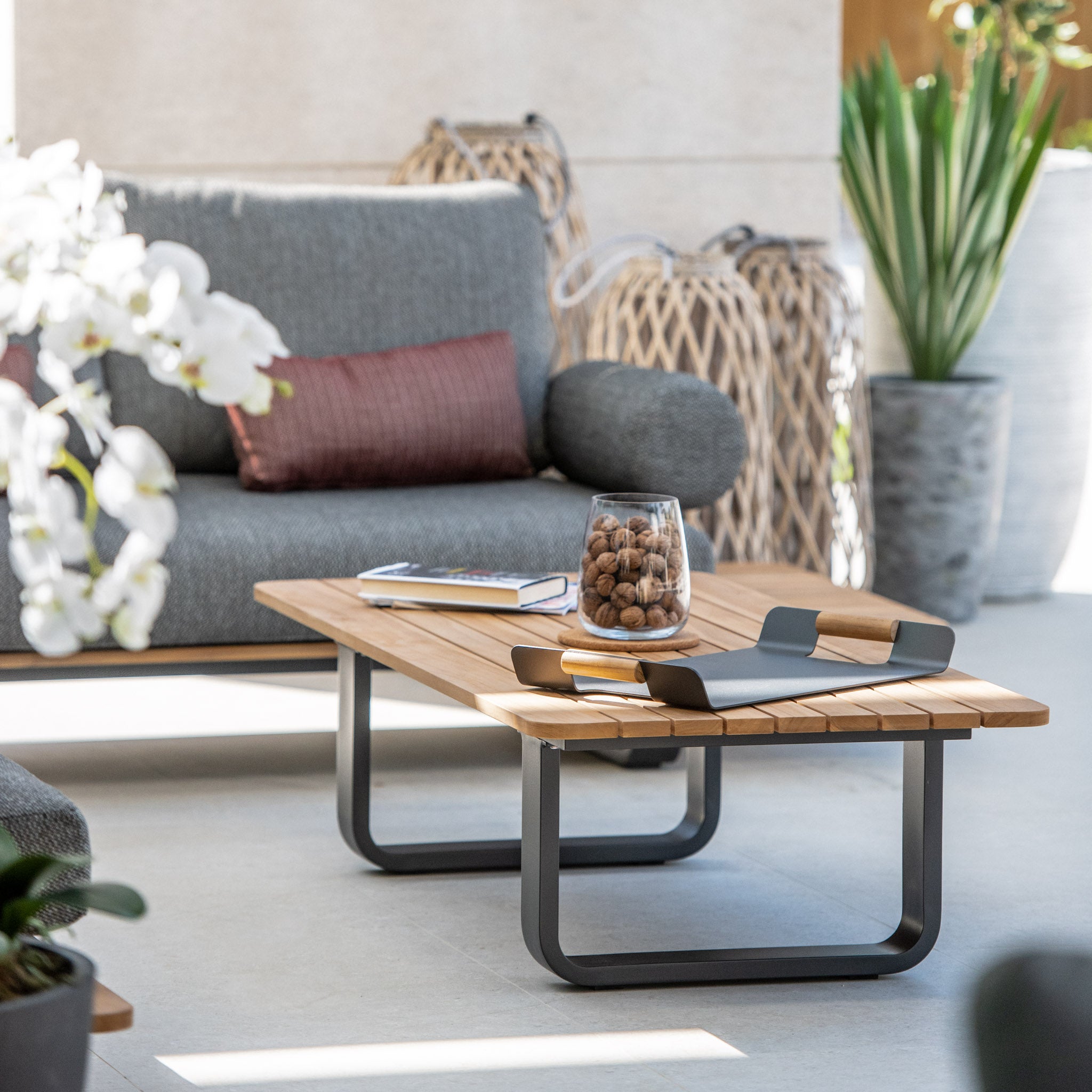 Modern living room with a Bay Large Corner Group Set in olive green, complemented by 4 waist pillows and a teak table, decorative plants, and ornaments in a bright, airy space.