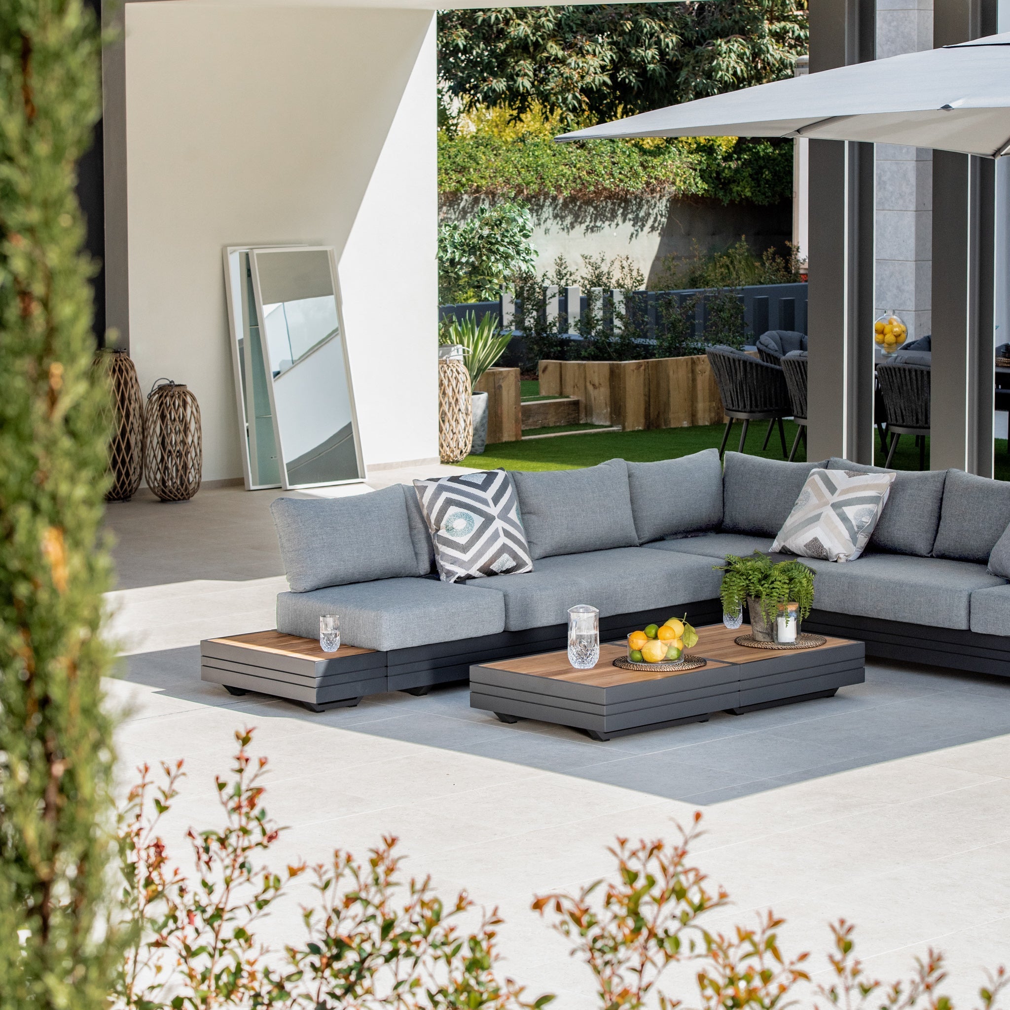 Modern outdoor patio featuring a Panama Luxury Outdoor Large Corner Group Set in Washed Grey, decorative pillows, and a coffee table adorned with lemons, limes, and a plant.