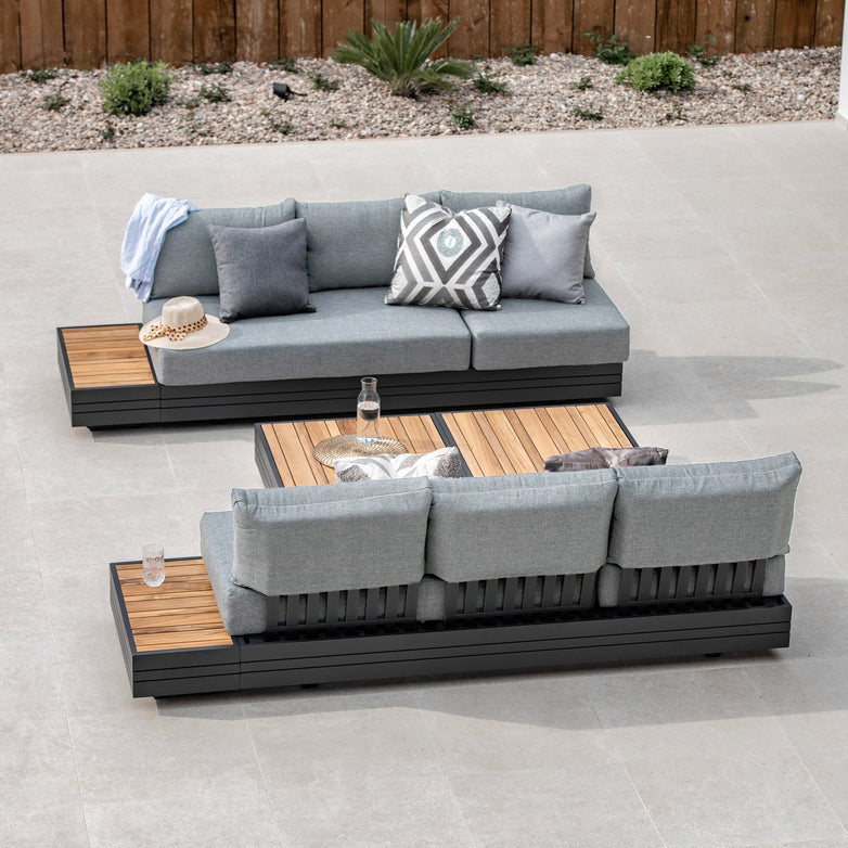 Outdoor seating arrangement featuring the Panama 3 Seat Sofa with Sun Lounger Feature in Washed Grey on a tiled patio, complemented by a wooden coffee table and sleek aluminum-framed loungers, creating an inviting oasis of stylish outdoor furniture.