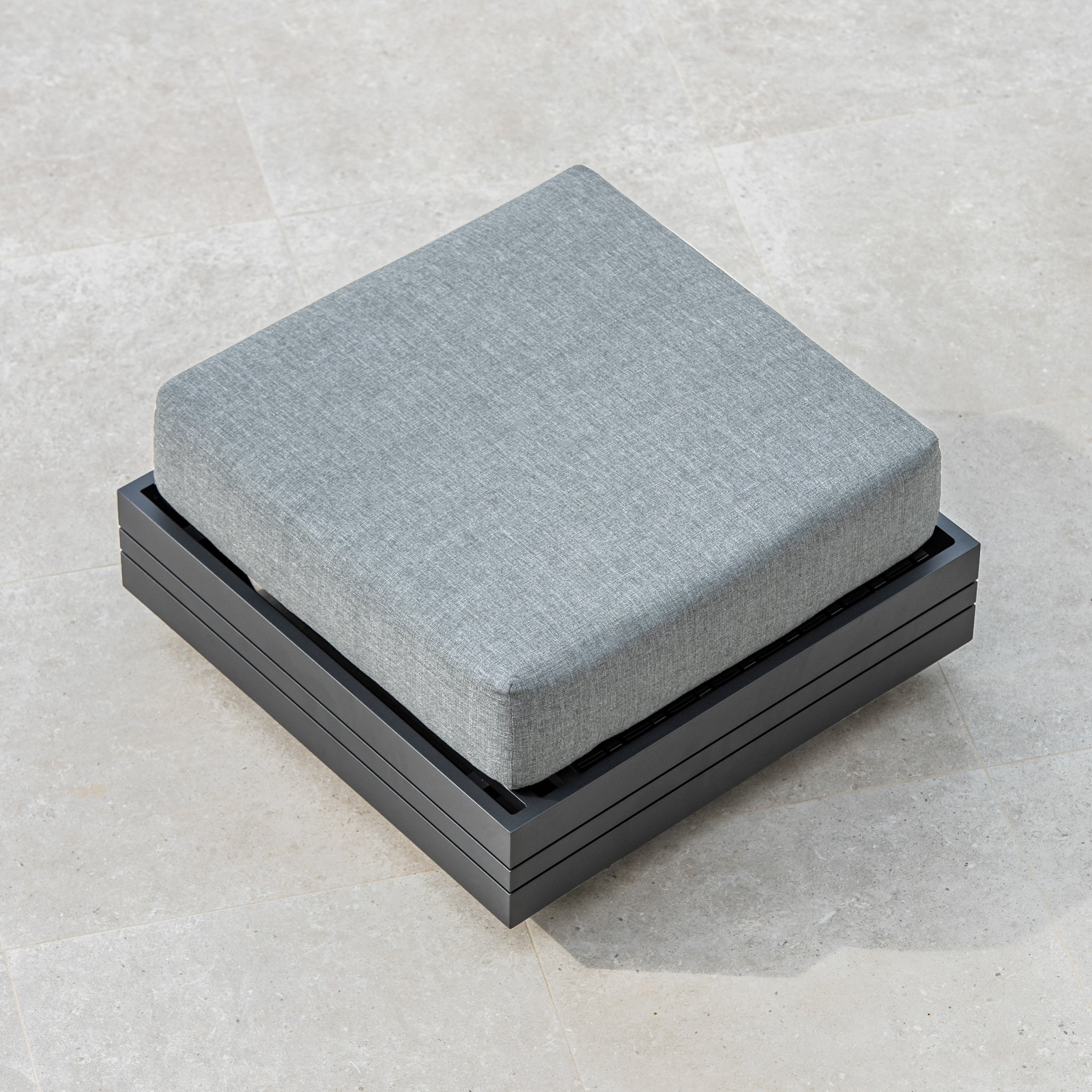 Washed grey cushion on a square, black, metal frame placed on a light-colored tiled floor, creating an inviting footstool as part of your Panama Corner Unit modular system.