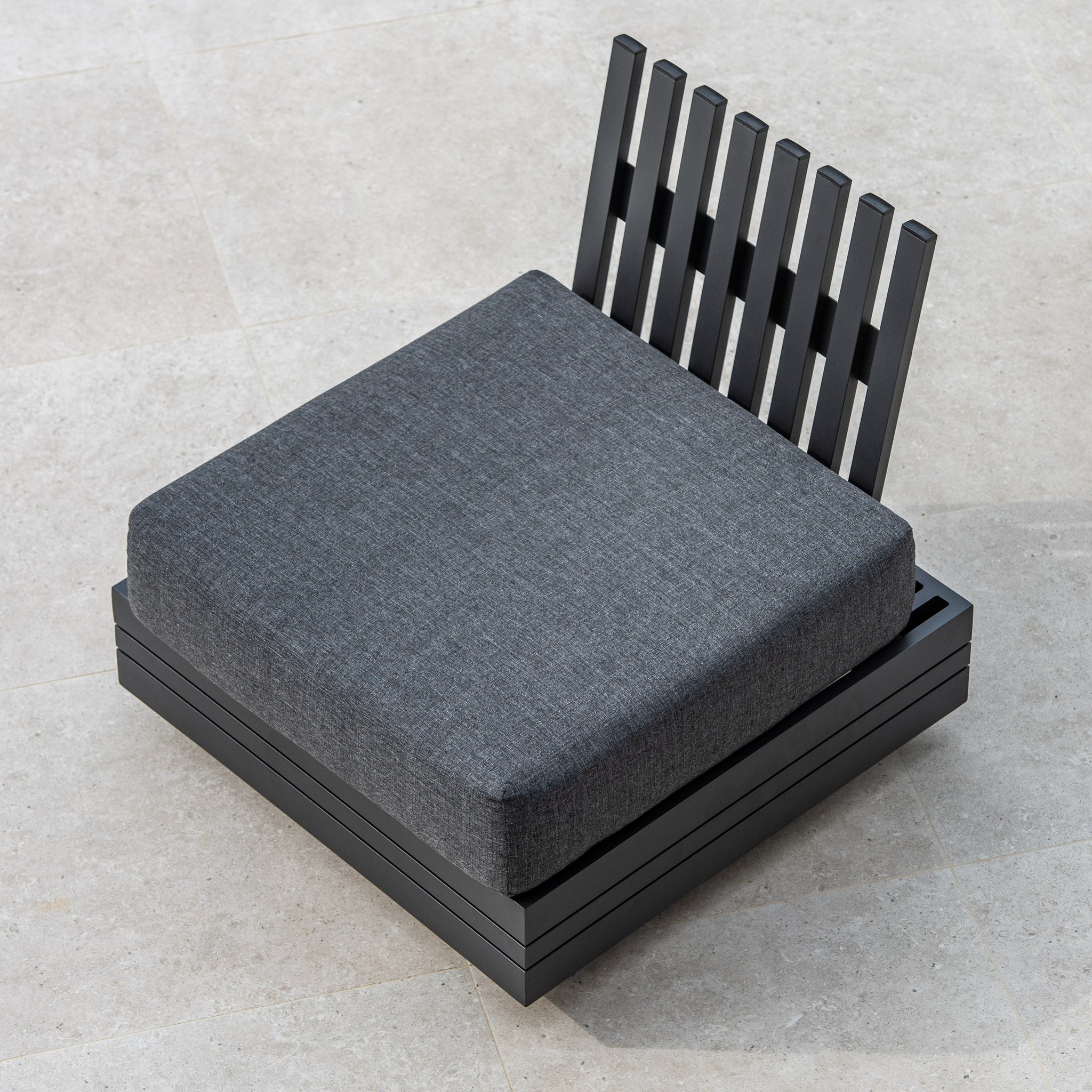 Panama Corner Unit/Footstool in Charcoal with a grey cushion and slatted backrest on a tiled floor, viewed from above. The stylish design seamlessly blends into any modular system.