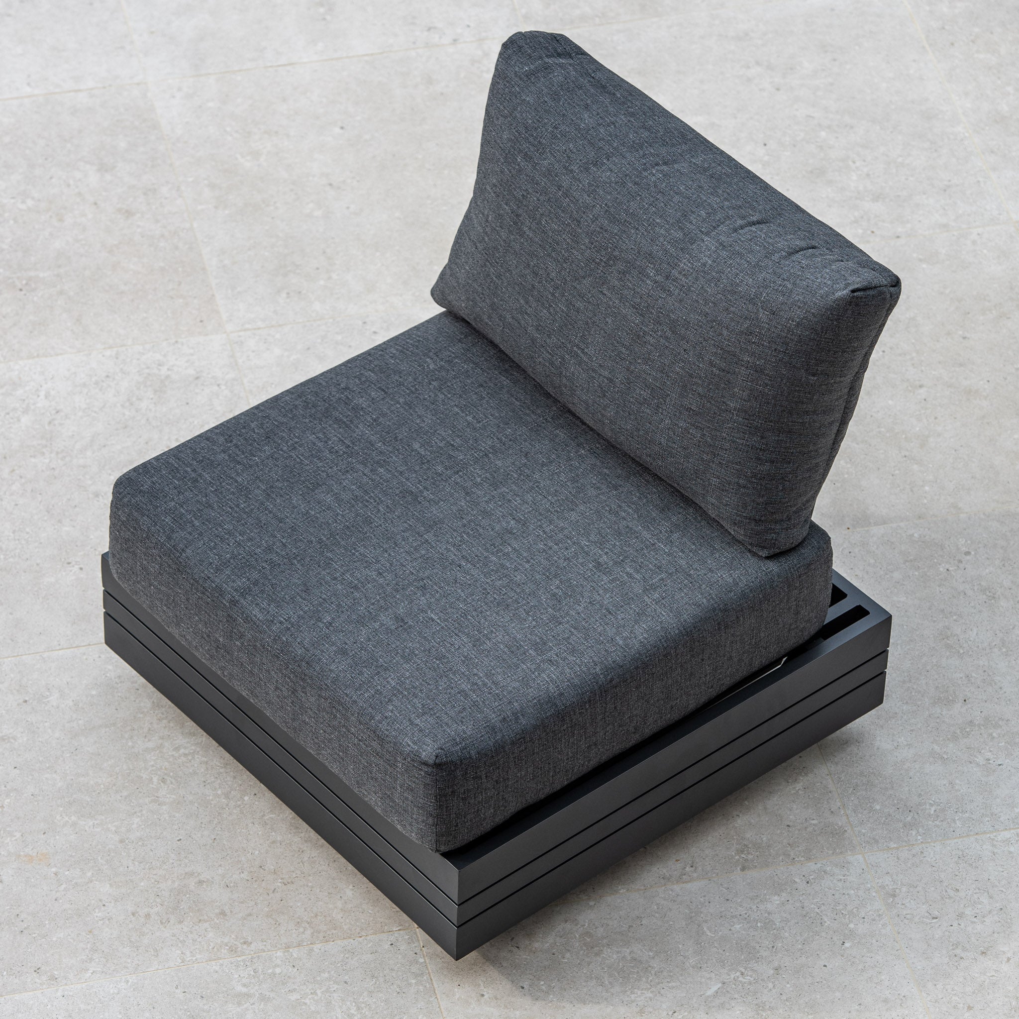 The Panama Corner Unit/Footstool in Charcoal, with its sleek design and black base, blends seamlessly into any modular system when viewed from above on a light grey tiled floor.