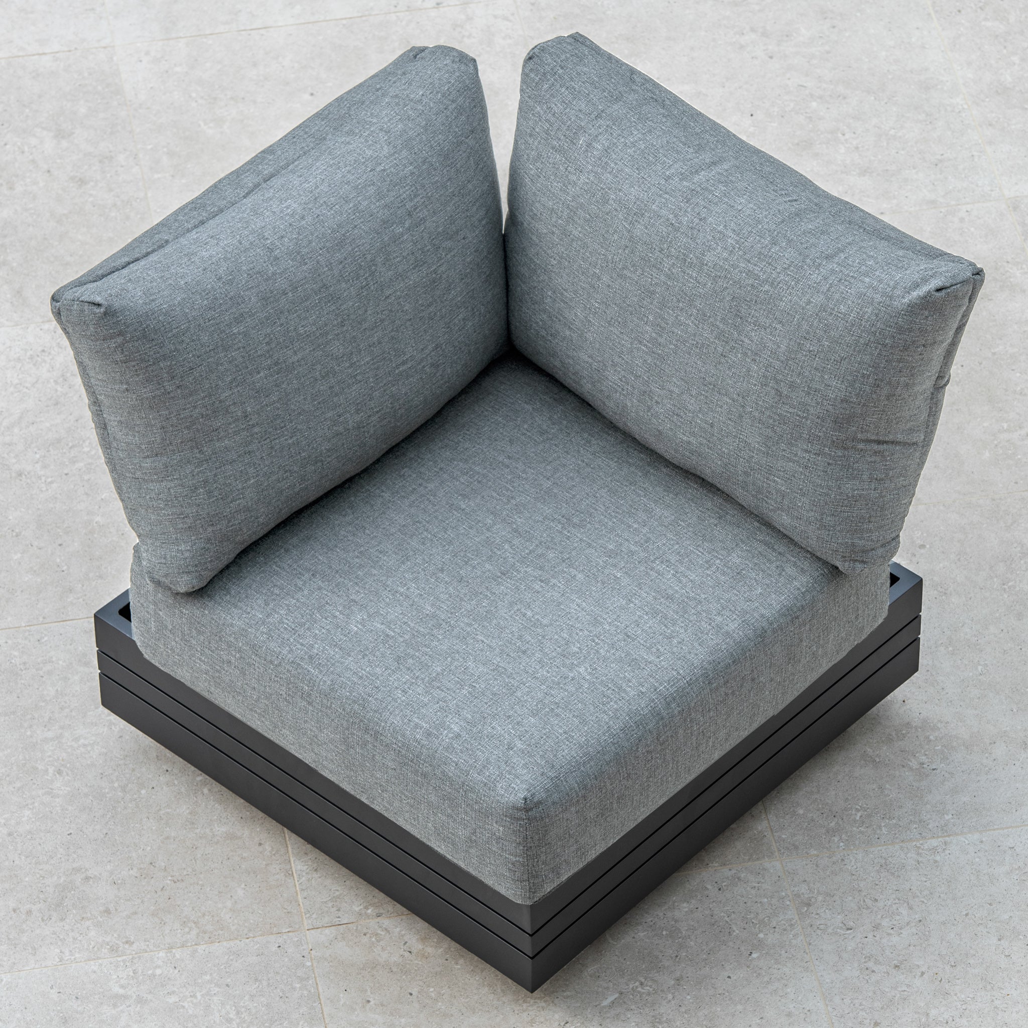 A Panama Corner Unit/Footstool in Washed Grey with a black wooden base sits elegantly on a light-colored tiled floor, offering both comfort and style as part of a versatile modular system.