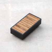 The contemporary rectangular bench features a wooden top and black sides, all set on a light-colored tiled surface. With its sleek aluminium frame, it seamlessly blends modern design with functionality, making it an ideal piece of outdoor furniture akin to the stylish Panama Teak Side Table.