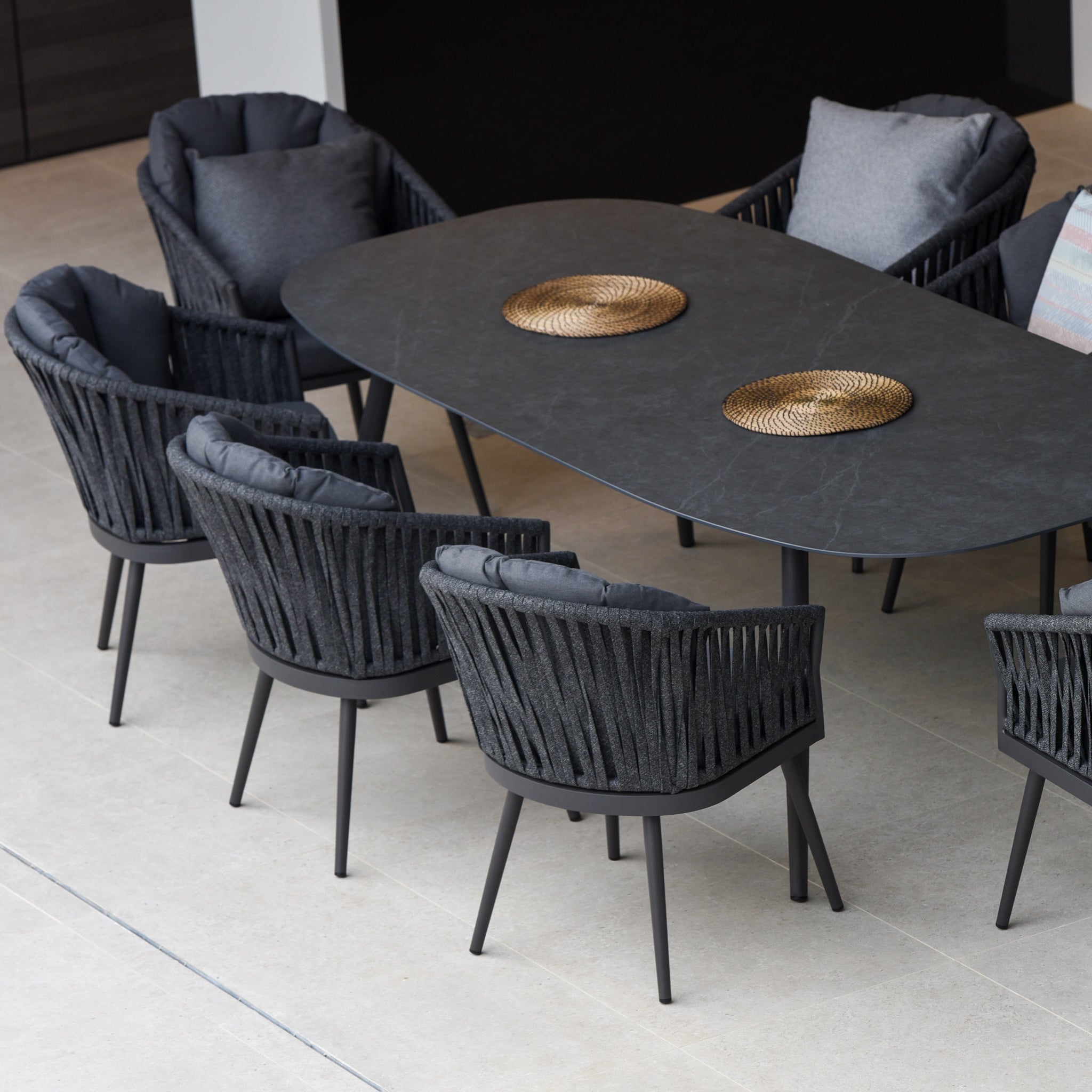 The Harbour Lifestyle Monterrey 8 Seat Rope Dining Set features a sleek grey oval ceramic dining table, eight cushioned outdoor rope dining chairs, and stylish round placemats.