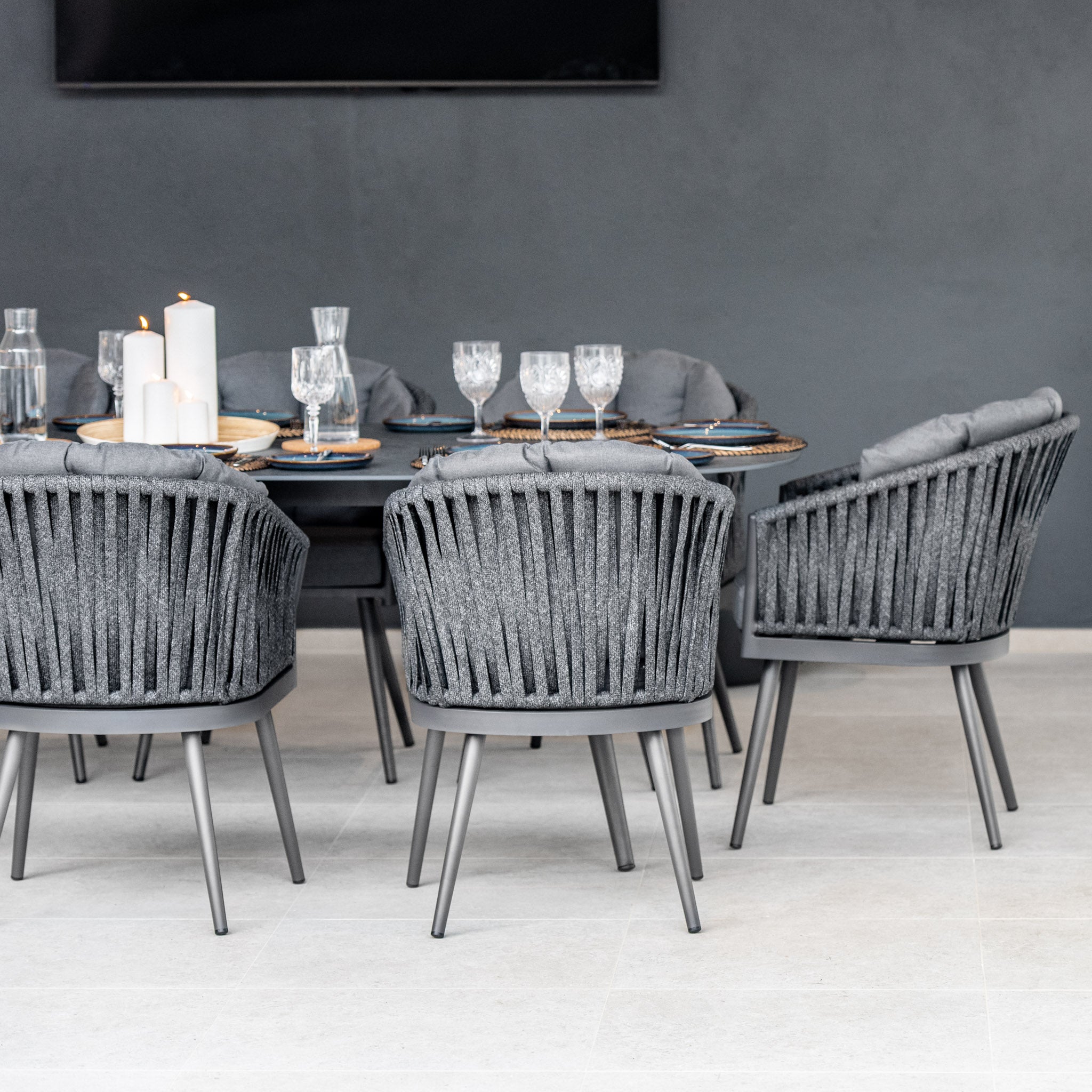 Modern dining area with a set table, featuring the Monterrey 8 Seat Rope Dining Set with Oval Ceramic Table in Grey, complete with gray cushions and decorative plate settings.