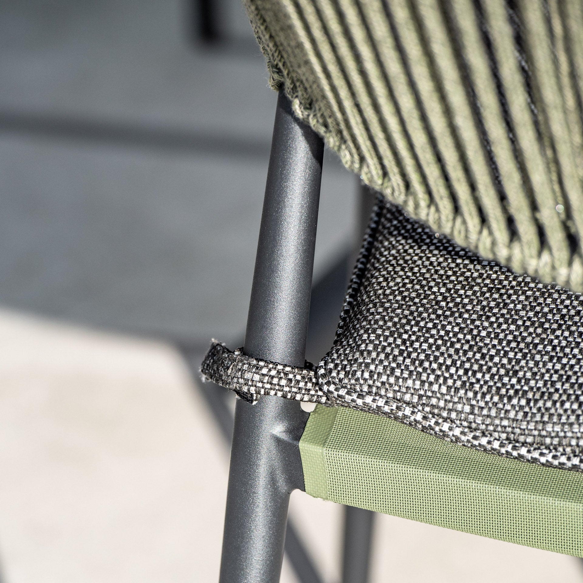 Close-up of the Cloverly 4 Seat Round Dining Set featuring a metal chair with green fabric and a textured black and white cushion, complete with a loop detail on the chair back, perfectly complementing the teak wood dining table top in Olive Green.