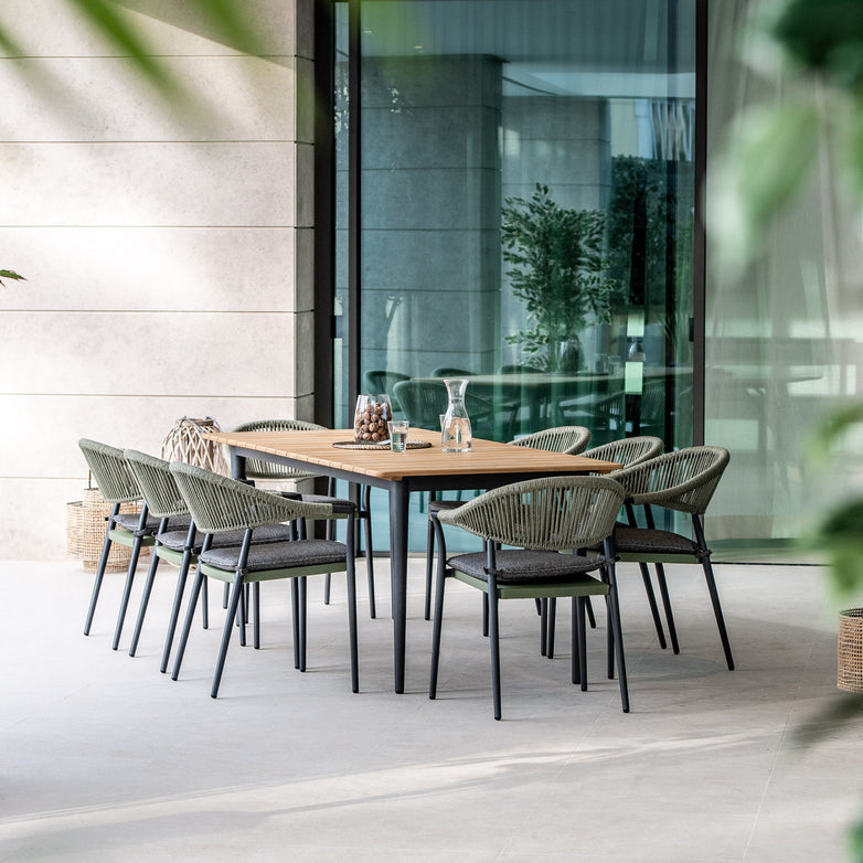 Modern outdoor dining area featuring the Cloverly 8 Seat Rectangular Dining with Teak Table in Olive Green, which includes a teak top and sleek aluminium frame. The wooden table and six chairs are elegantly decorated with vases and surrounded by lush greenery.