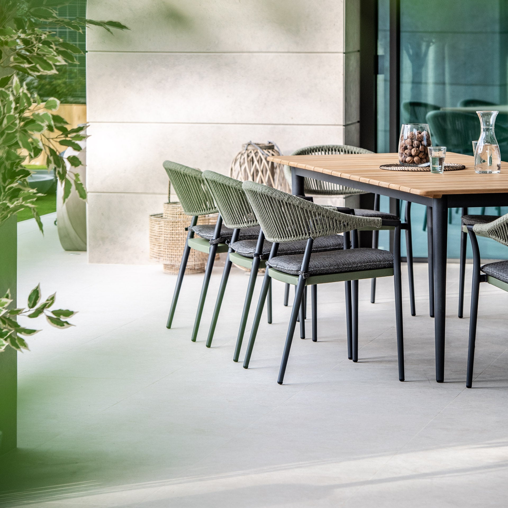 Modern outdoor dining area featuring the Cloverly 8 Seat Rectangular Dining with Teak Table in Olive Green, complemented by six matching chairs and a glass of water on the table.