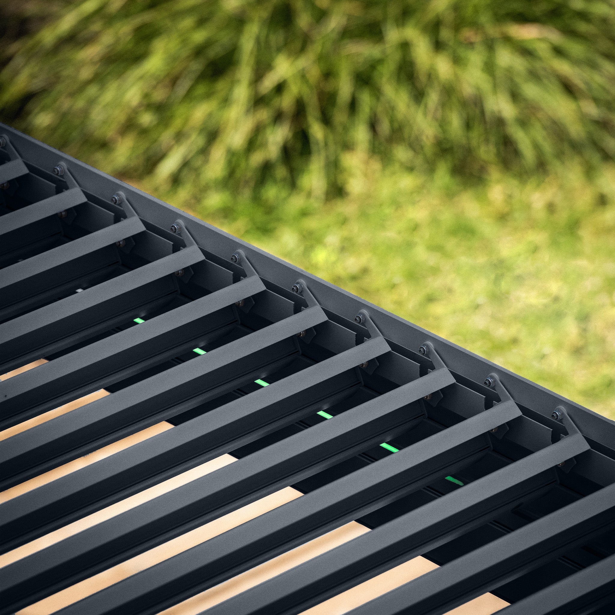 Close-up of the PergoSTET Plus grey pergola, featuring a louvred roof with parallel slats, set against blurred green grass.