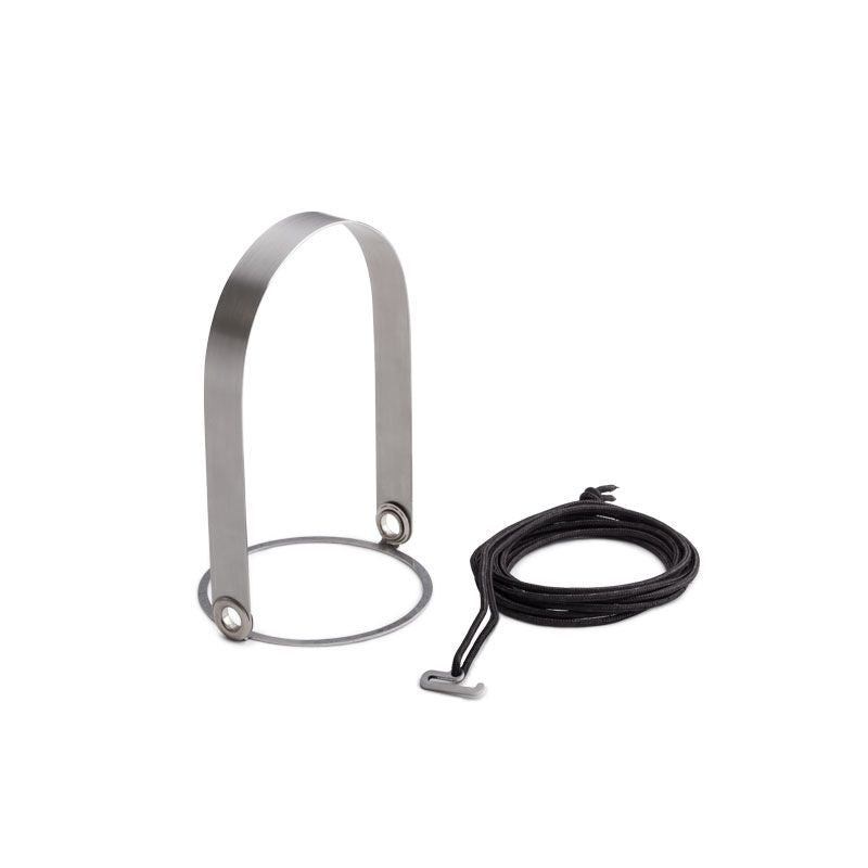 The Höfats GRAVITY CANDLE Hanger features a brushed solid stainless steel buckle with a circular base, accompanied by a black rope and a small T-shaped metal tool.