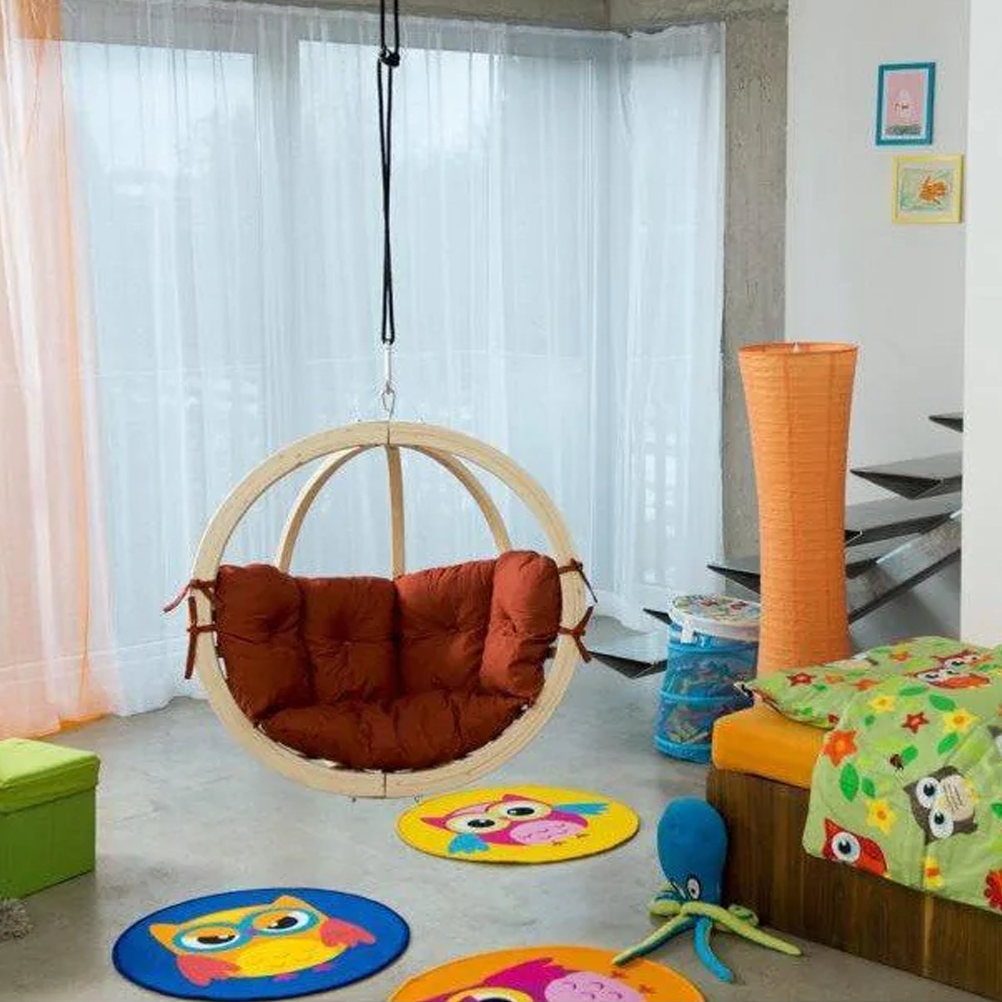 A vibrant children's room featuring a comfortable Natura Globo Single Hanging Chair, owl-themed decor, and playful rugs on the floor.