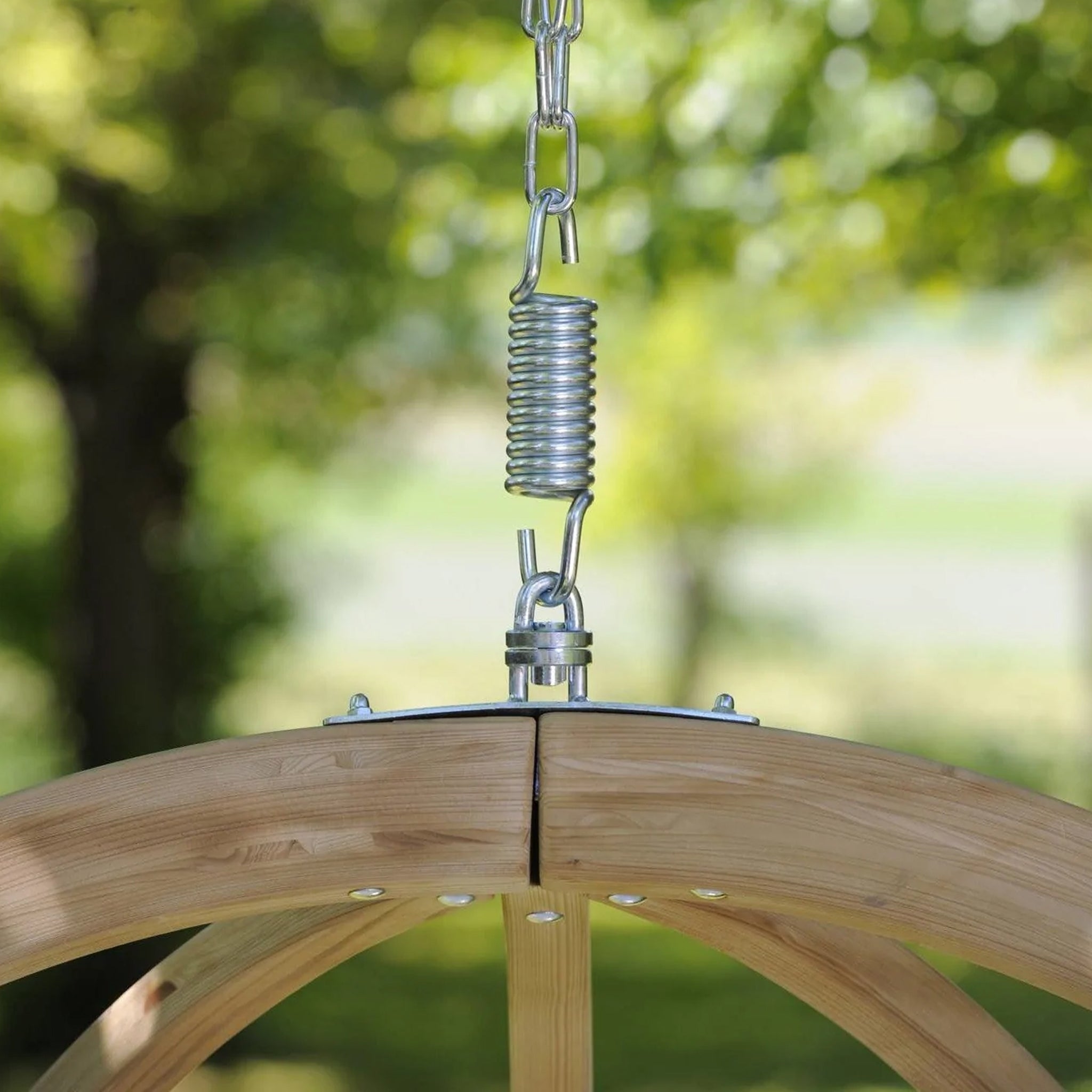 Close-up of the Natura Globo Single Hanging Chair, a stylish wooden swing connected by metal chains and a spring, perfect for indoor and outdoor living spaces in a green outdoor setting.
