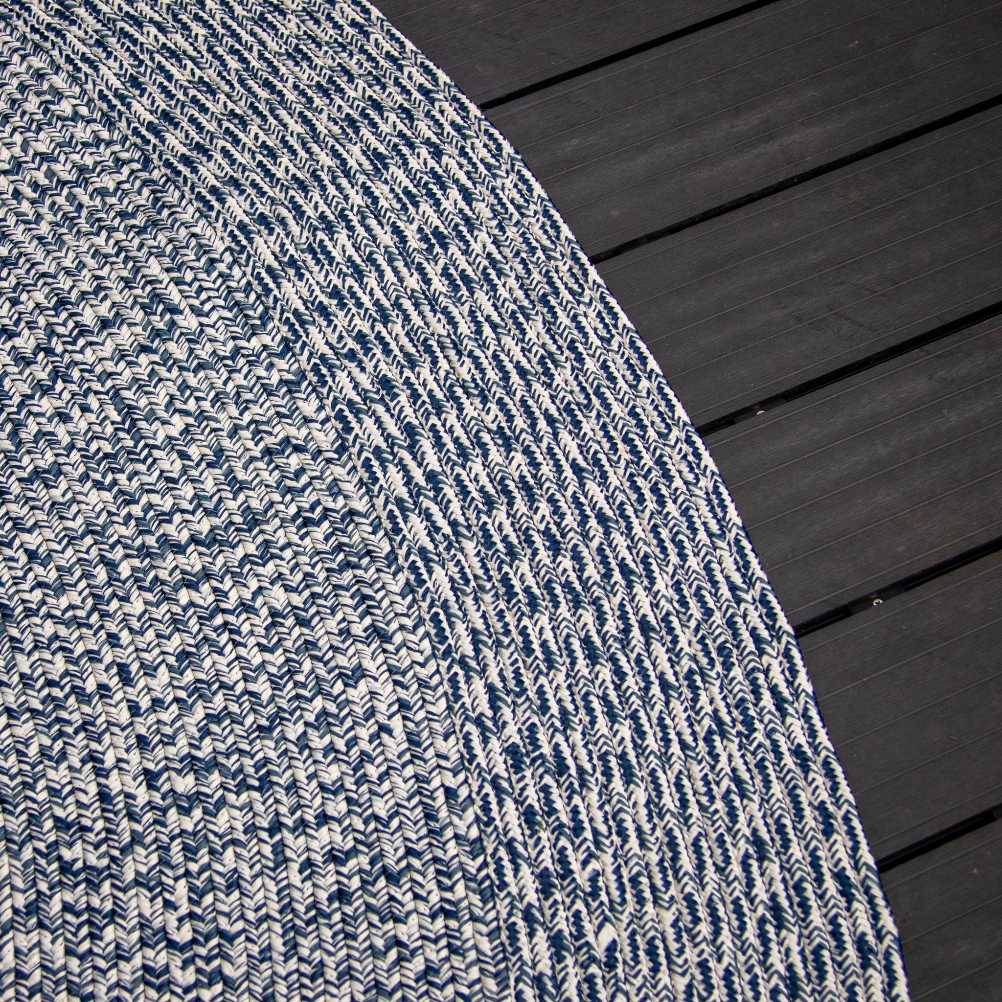 Close-up of the Apollo 300cm Round Indoor and Outdoor Rug in Prussian Blue, showcasing its woven blue and white circular design that is UV resistant and weatherproof, partially covering dark gray wooden flooring.