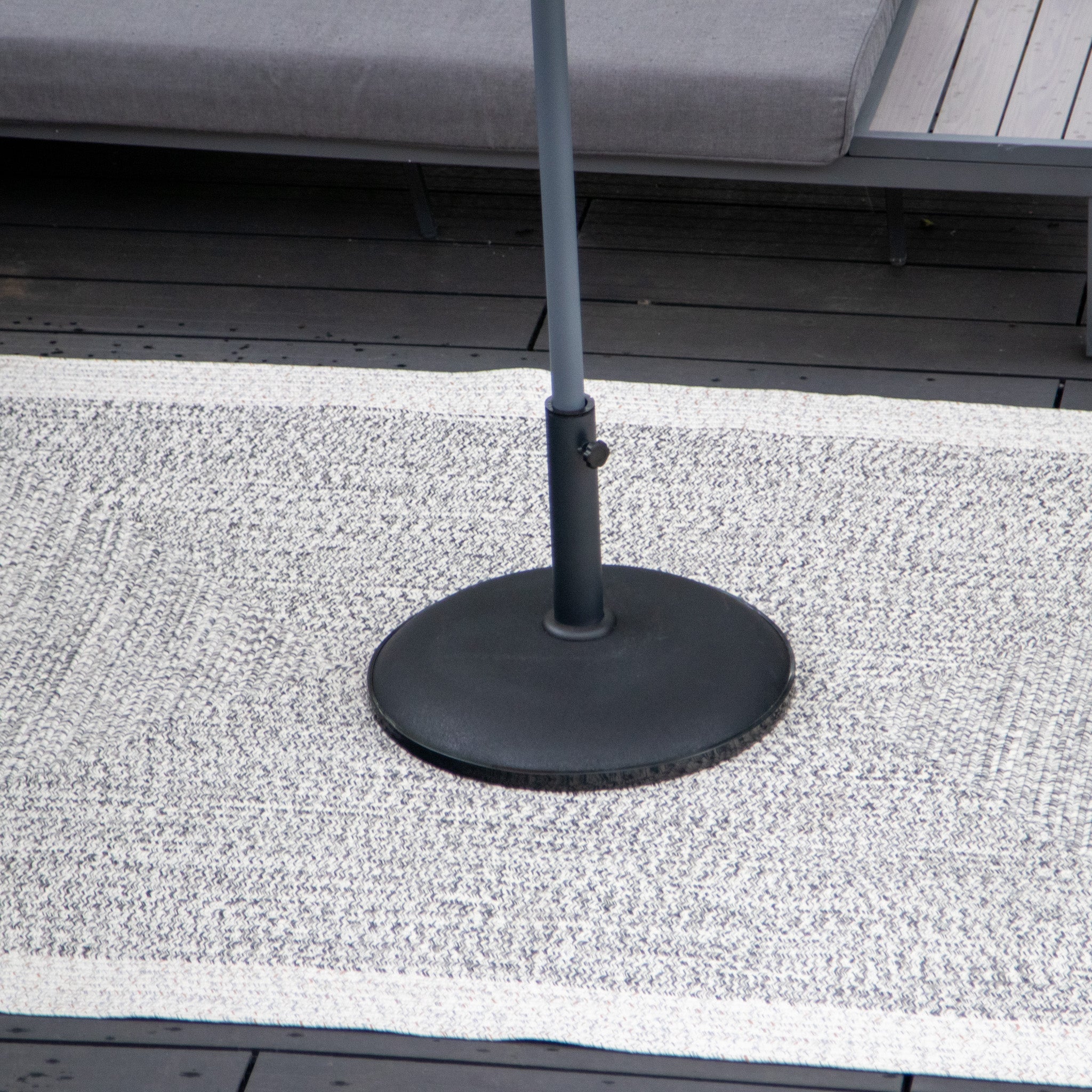 Base of an umbrella stand on a Hades 290cm x 190cm Weatherproof Indoor and Outdoor Rug in Cobble Grey with a UV resistant sectional sofa in the background.